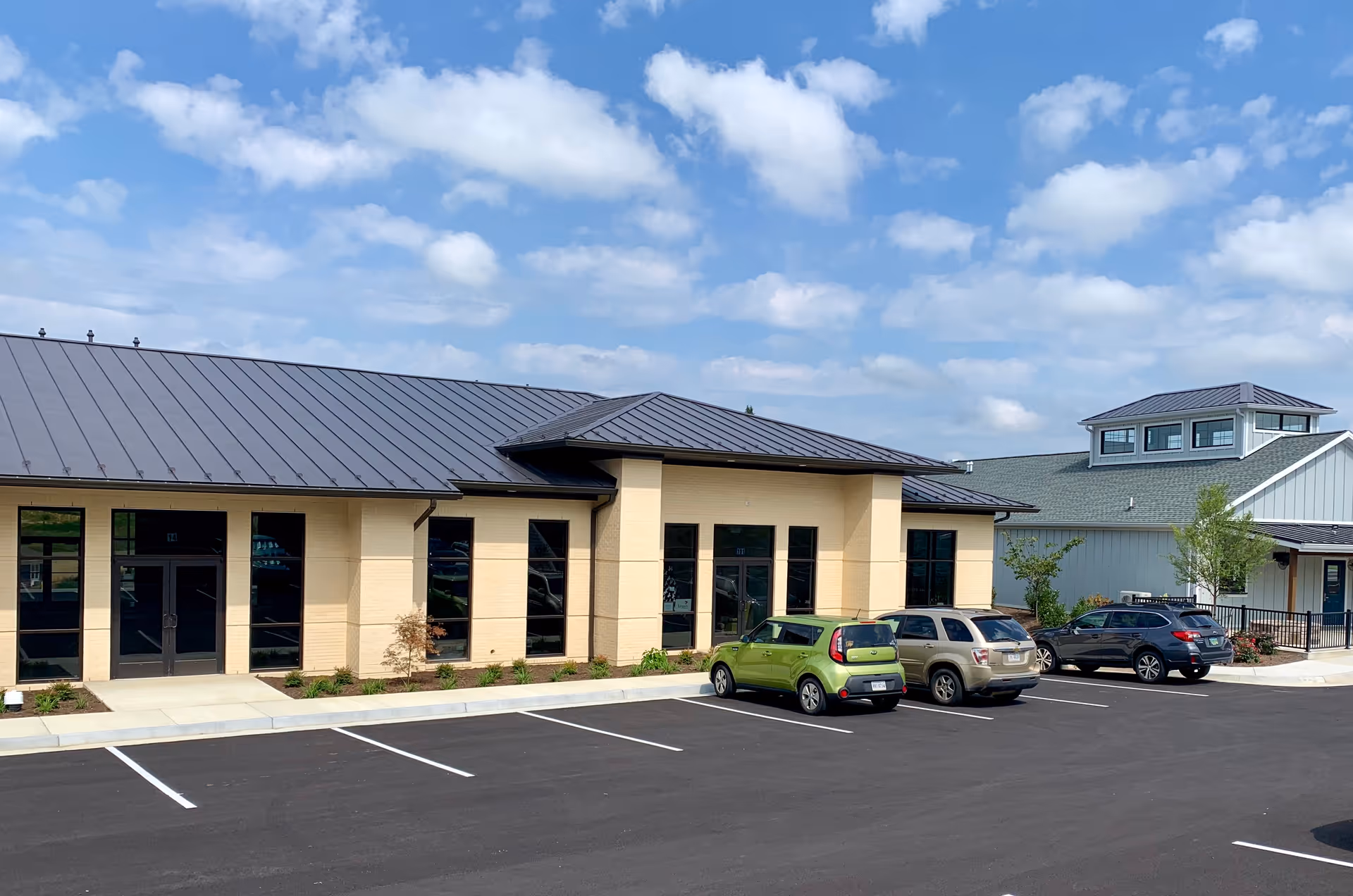 Exterior view of a beige senior living facility with a dark metal roof and parked cars.