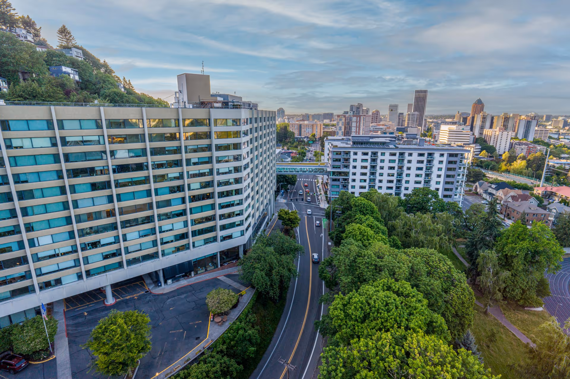 Aerial view of the Terwilliger Plaza Retirement Community building next to a tree-lined road with nearby apartments and the city skyline in the background.