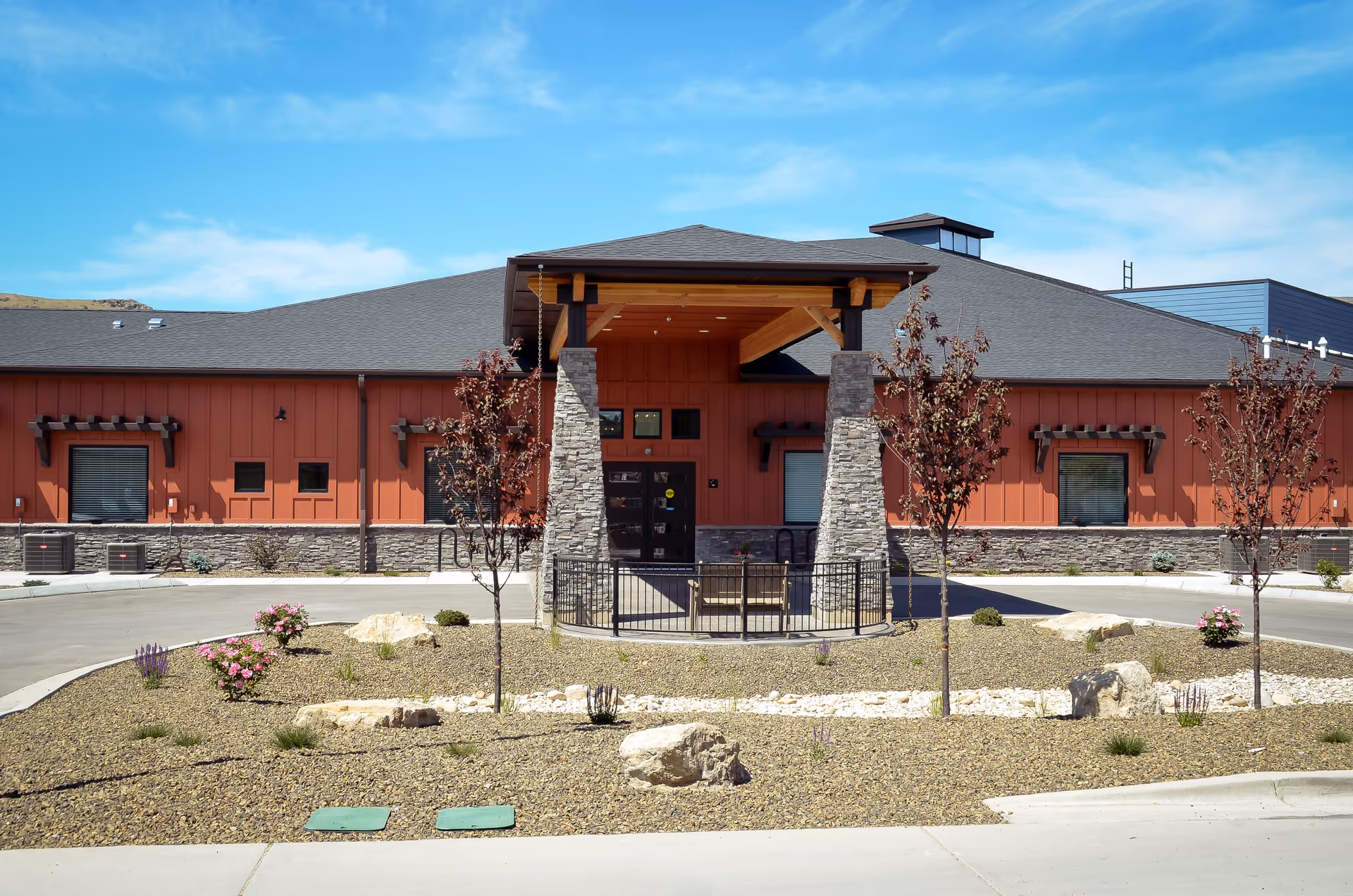 Front exterior of Aspen Valley Senior Living showing a single-story building with a covered entrance supported by stone columns and a landscaped circular driveway.