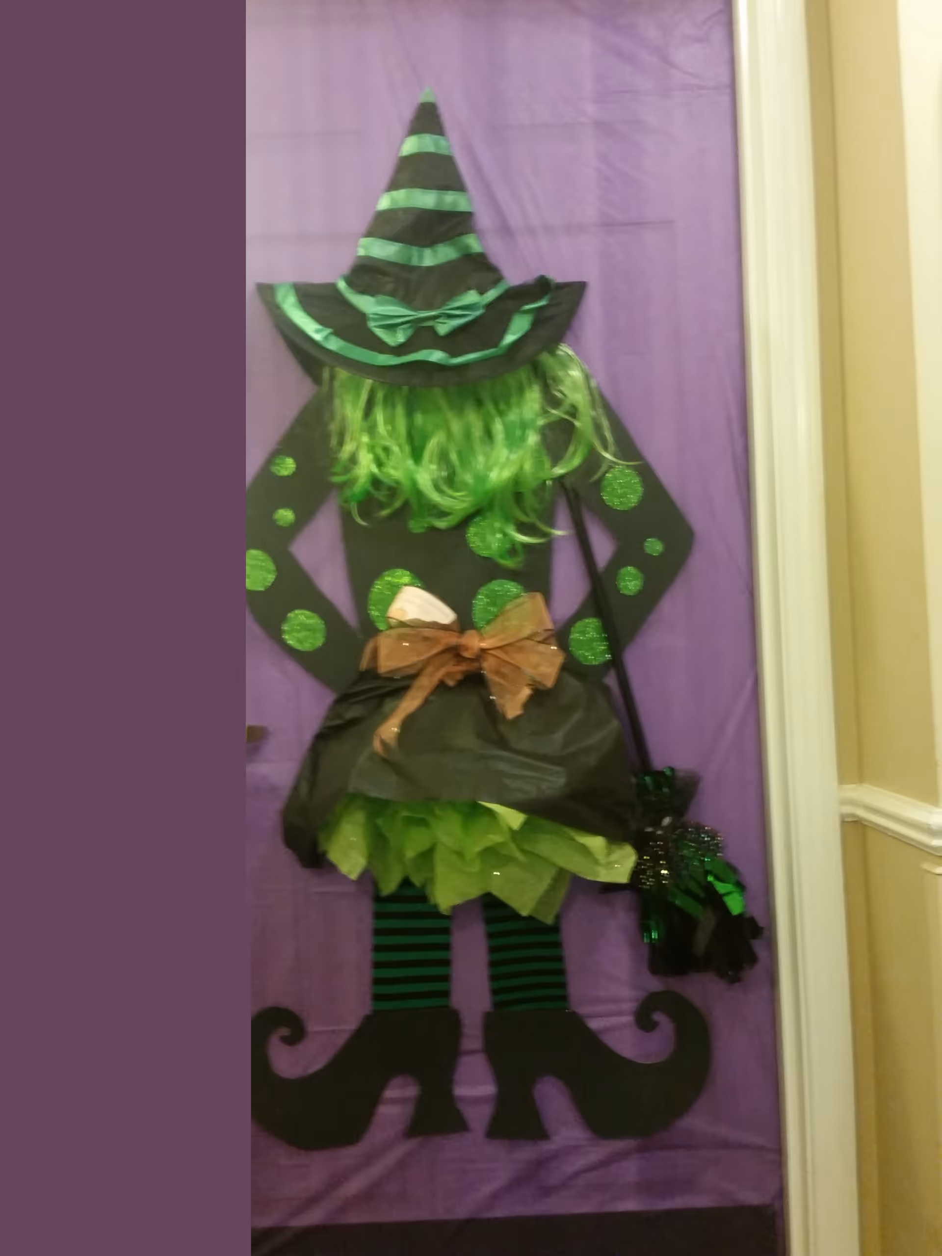 Interior view of a purple wall with a green witch Halloween decoration.
