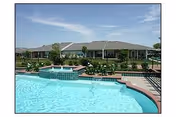 Outdoor pool area with lounge seating and a single-story building behind landscaped grounds.