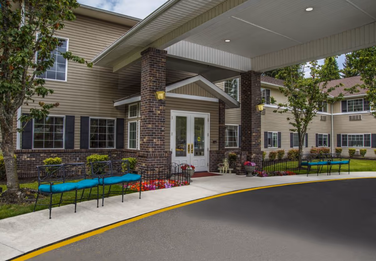 Exterior view of Normandy Park Senior Living entrance with brick columns and benches along the walkway.
