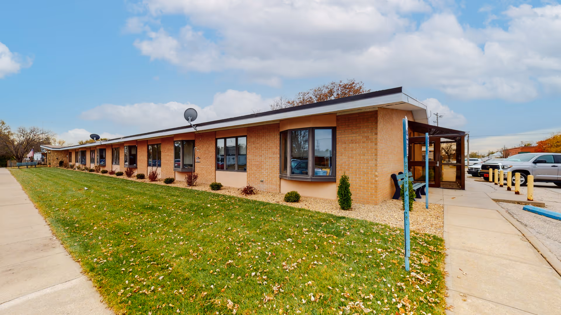 Single-story brick facility exterior with lawn, sidewalk, and parked cars.