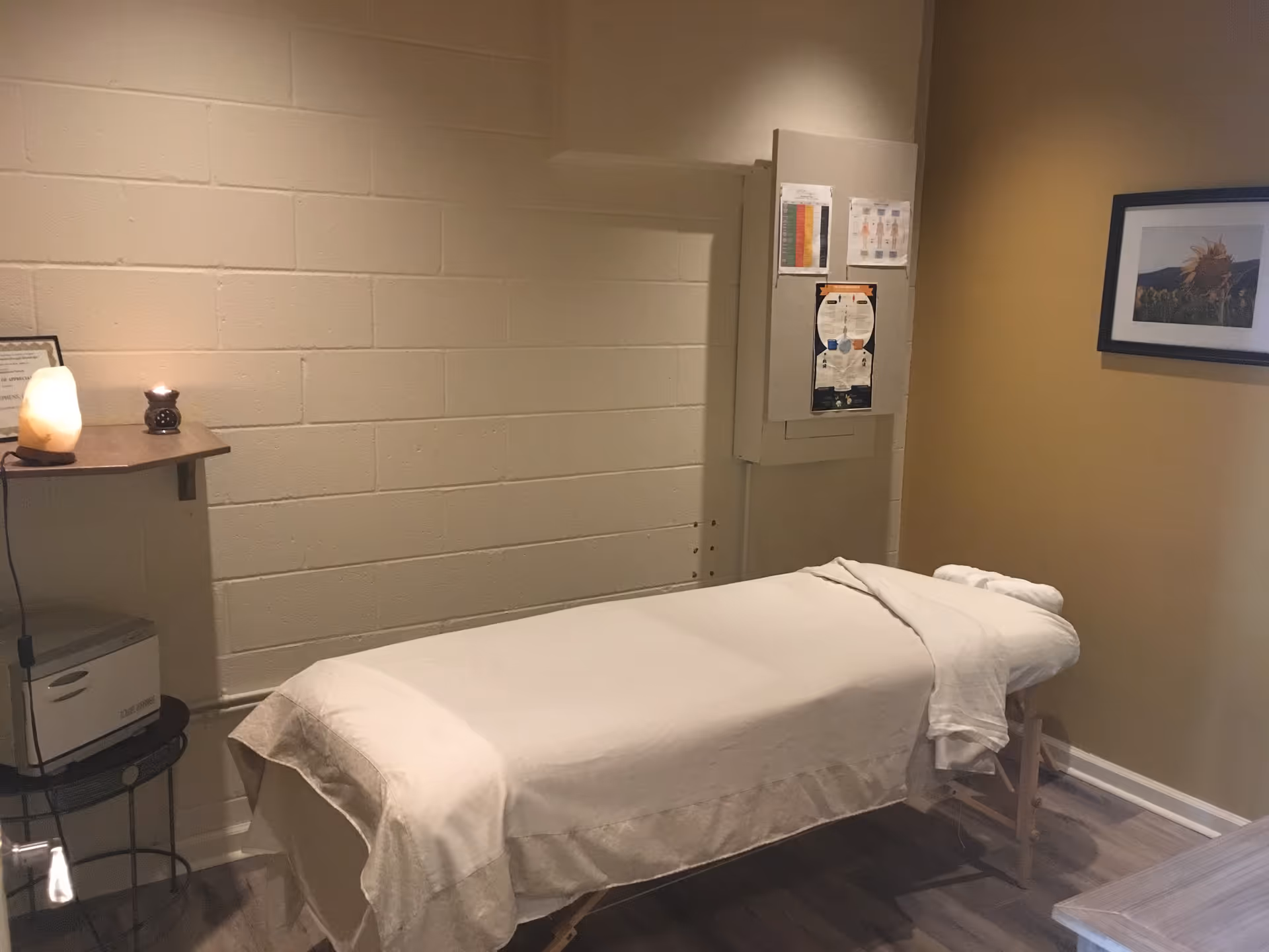 Massage room with a covered table, salt lamp, and framed wall art.