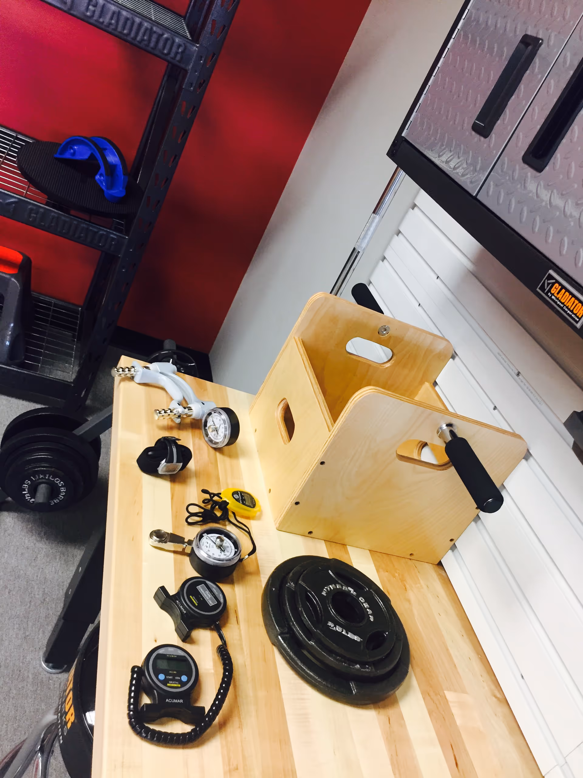 Wooden table with gym gear, scales, and a storage box in a gym corner.