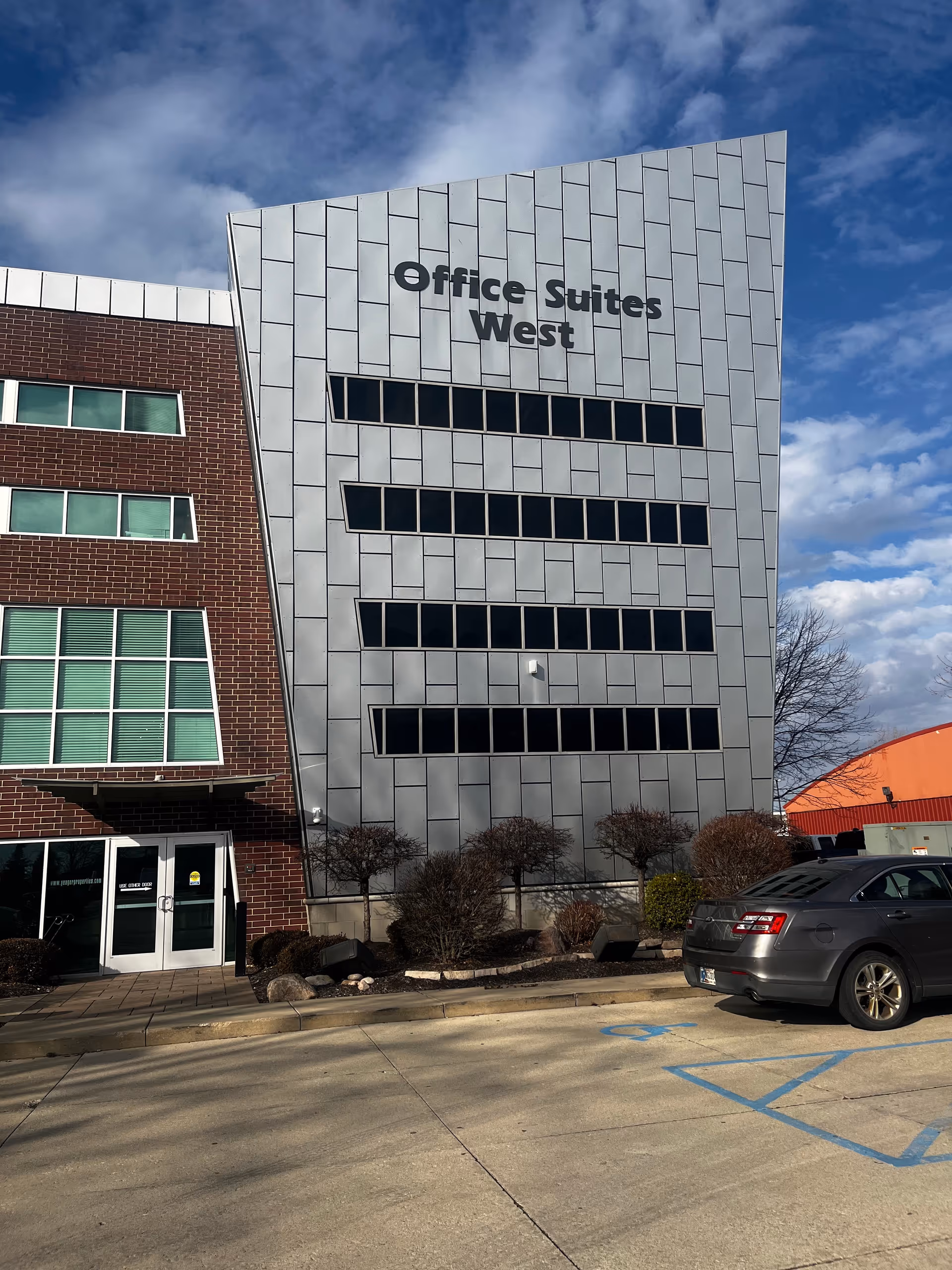 Exterior view of a modern office building labeled Office Suites West with a parked car nearby