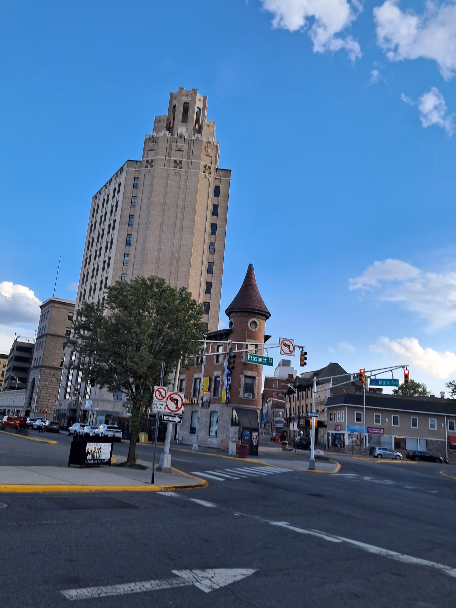 Urban intersection with tall beige skyscraper, turreted brick building, and blue sky.