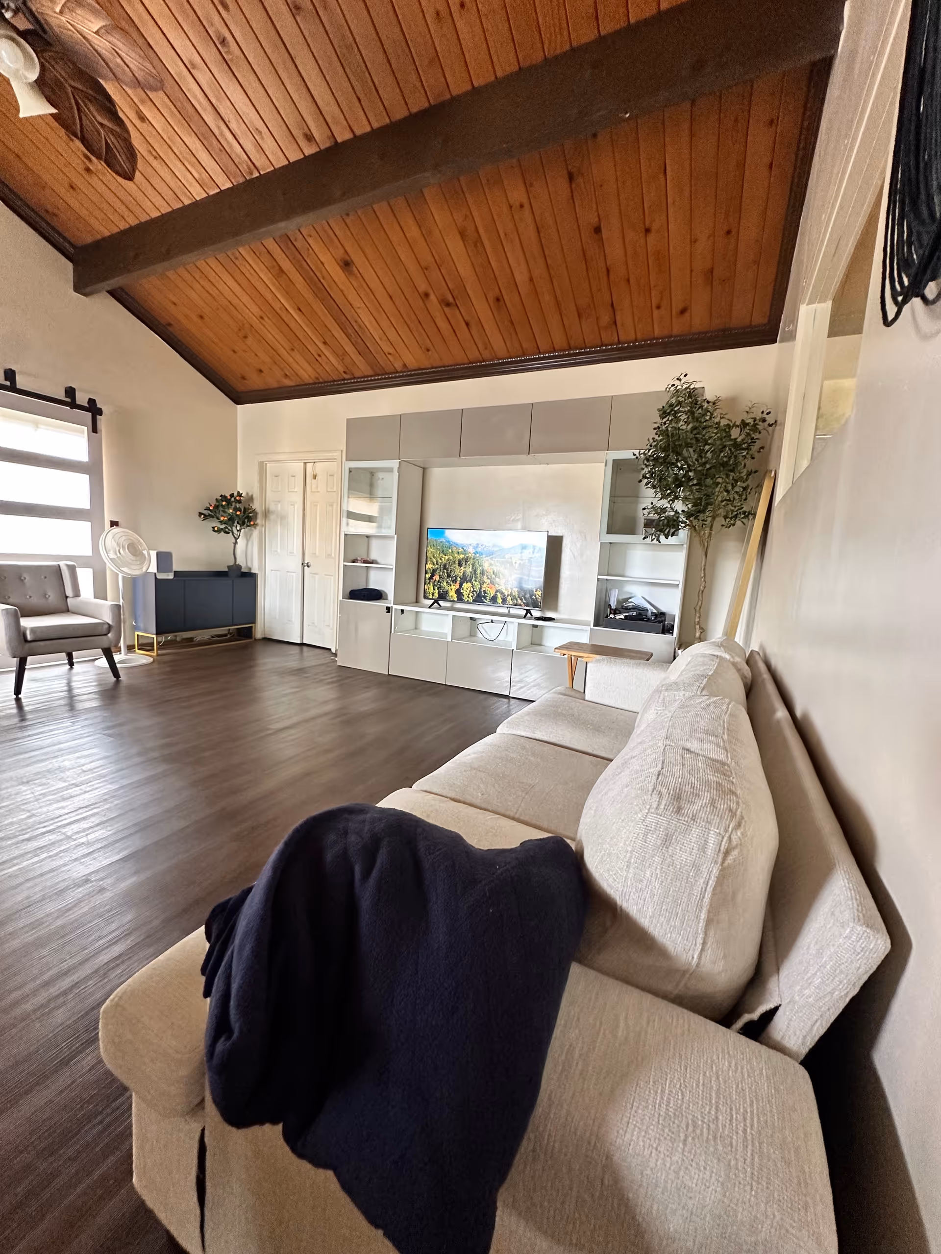 Spacious living room with beige sofa, wood ceiling beams, and TV unit.