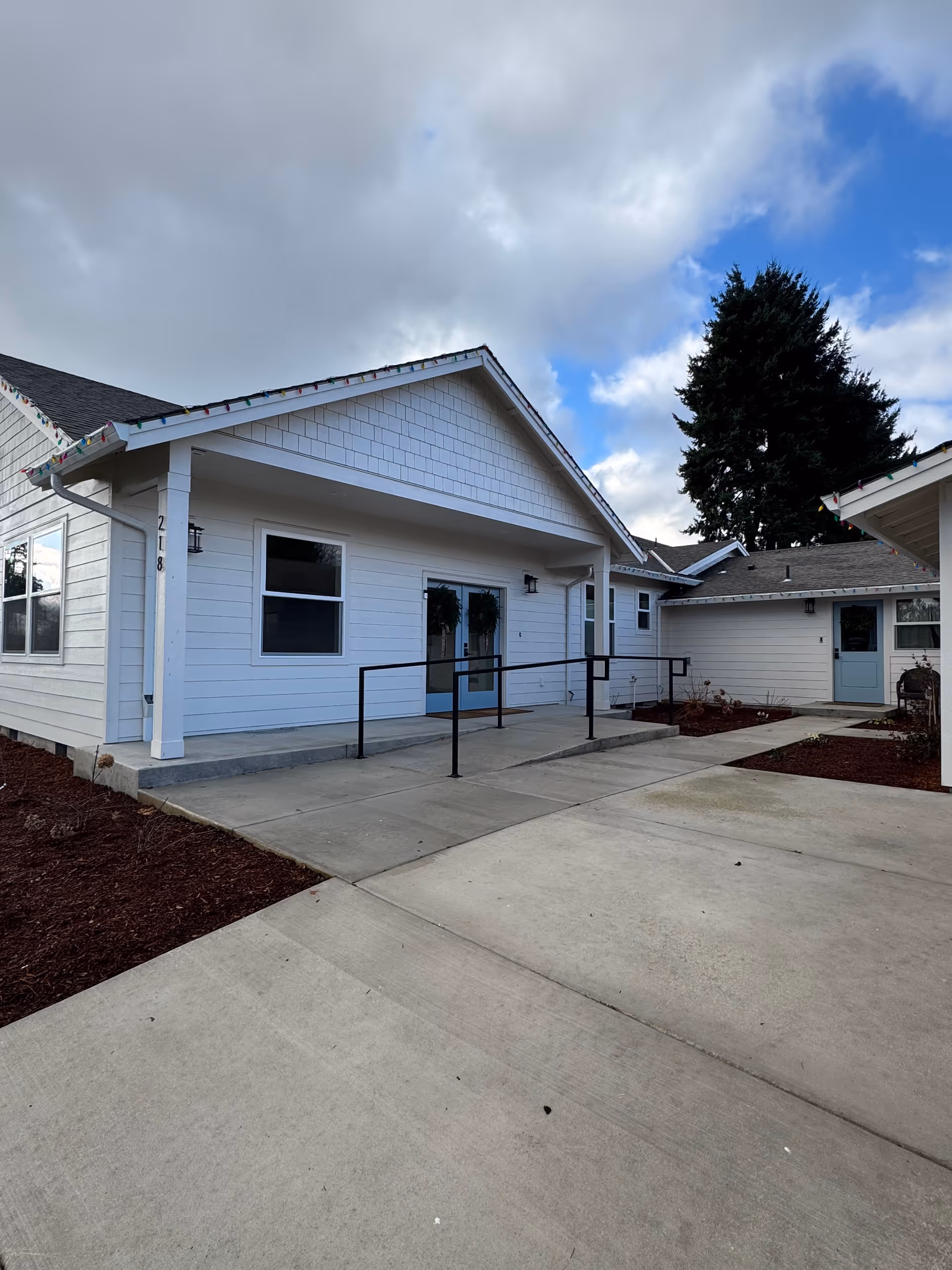 White, single-story senior living facility exterior with a ramped entrance and blue doors.