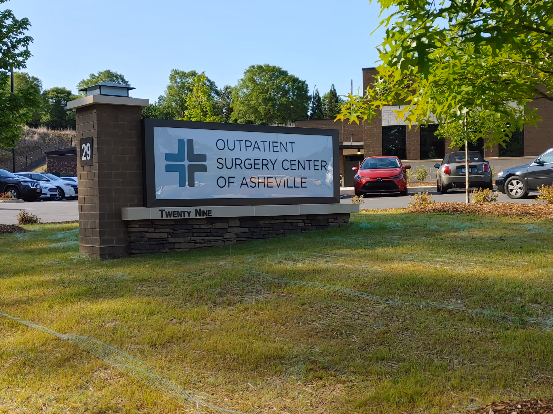 Front exterior sign for Outpatient Surgery Center of Asheville with parked cars nearby.