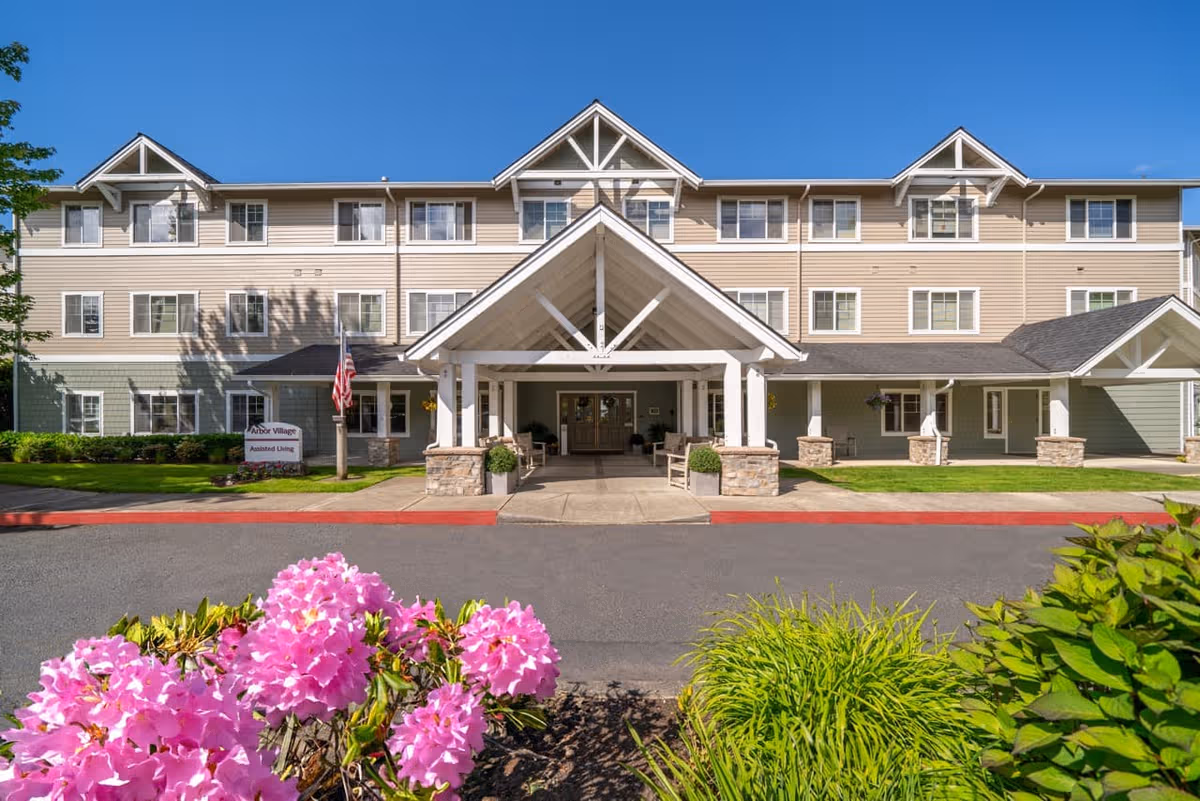 Exterior view of Arbor Village Senior Living with a covered entrance and pink flowers in foreground.