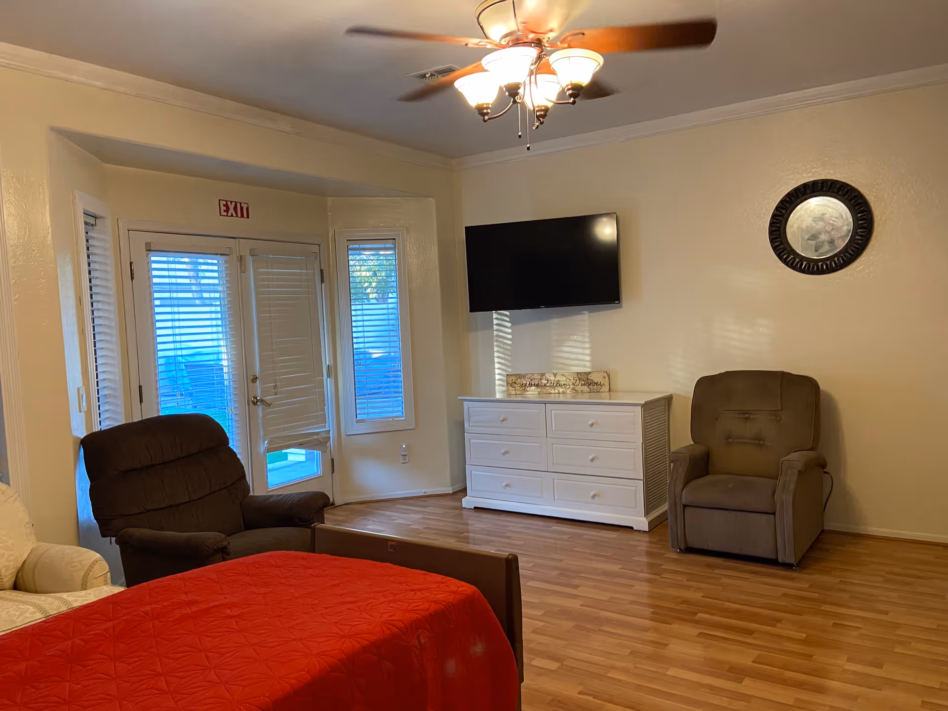 A cozy living room with recliners, a dresser, TV, ceiling fan, bed, and exit door.