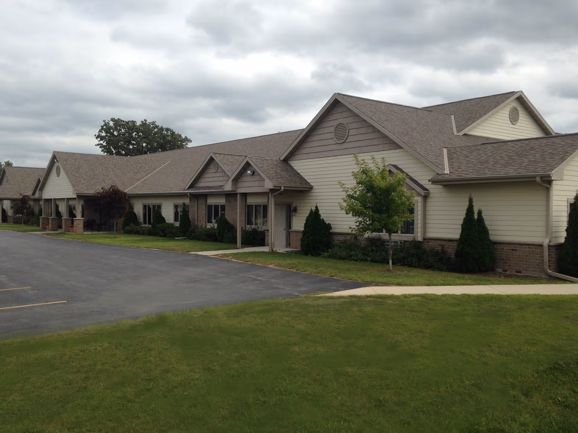 Single-story senior living facility with beige siding, gabled roof, and well-kept lawn.