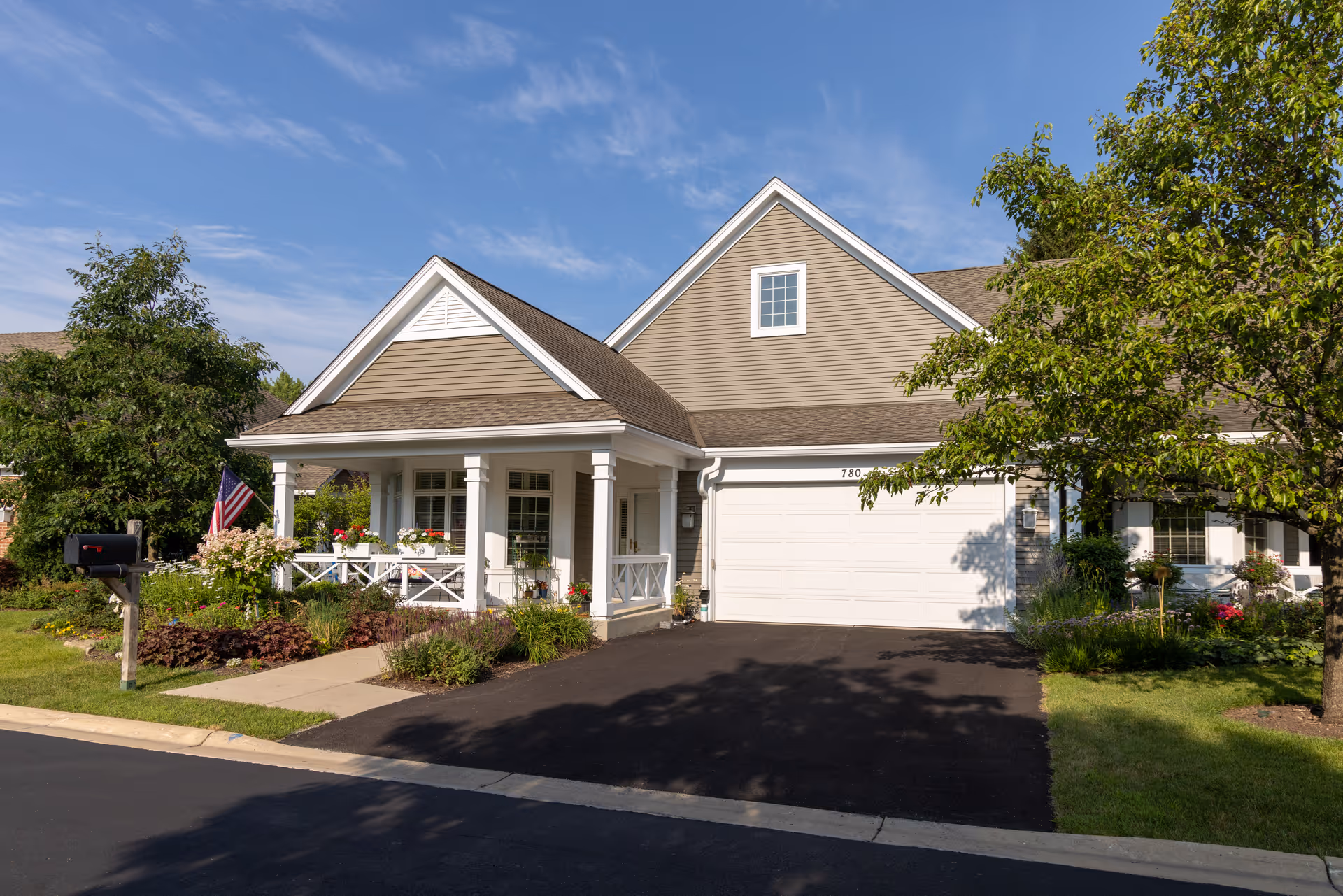 Single-story beige house with a covered front porch, attached garage, driveway, mailbox and landscaped yard.
