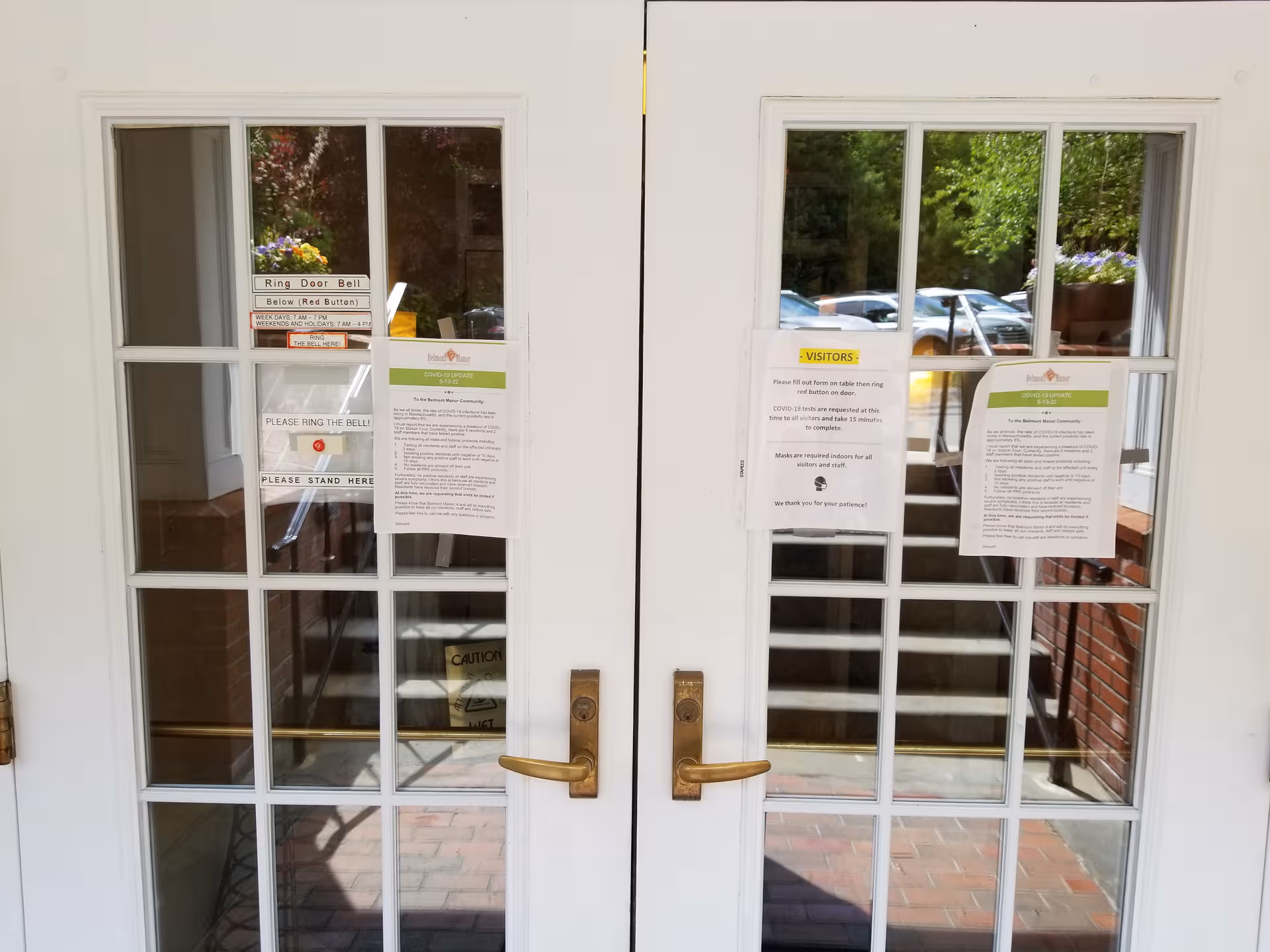 White double doors with glass panes and posted notices at the Belmont Manor entrance.
