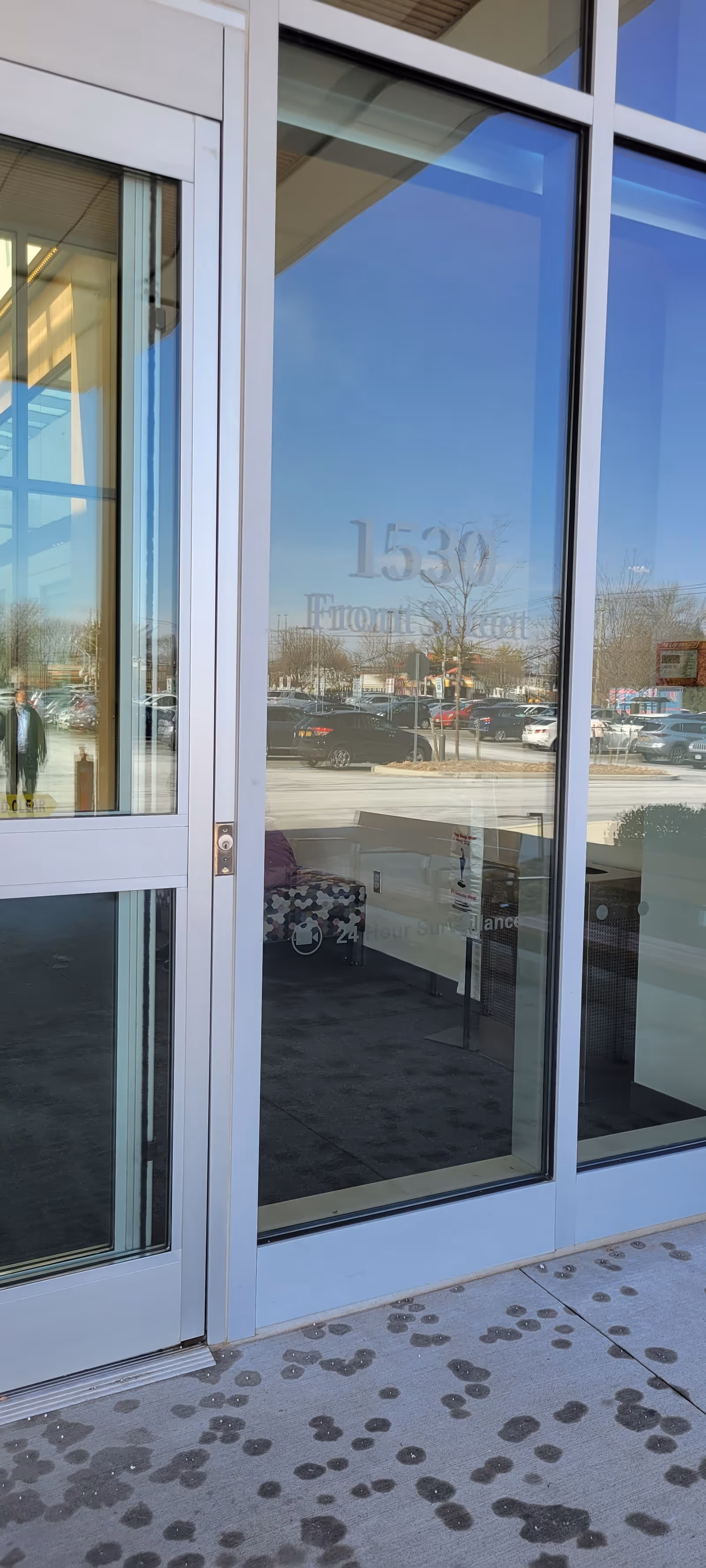 Glass entrance doors of a medical facility reflect a parking lot outside.