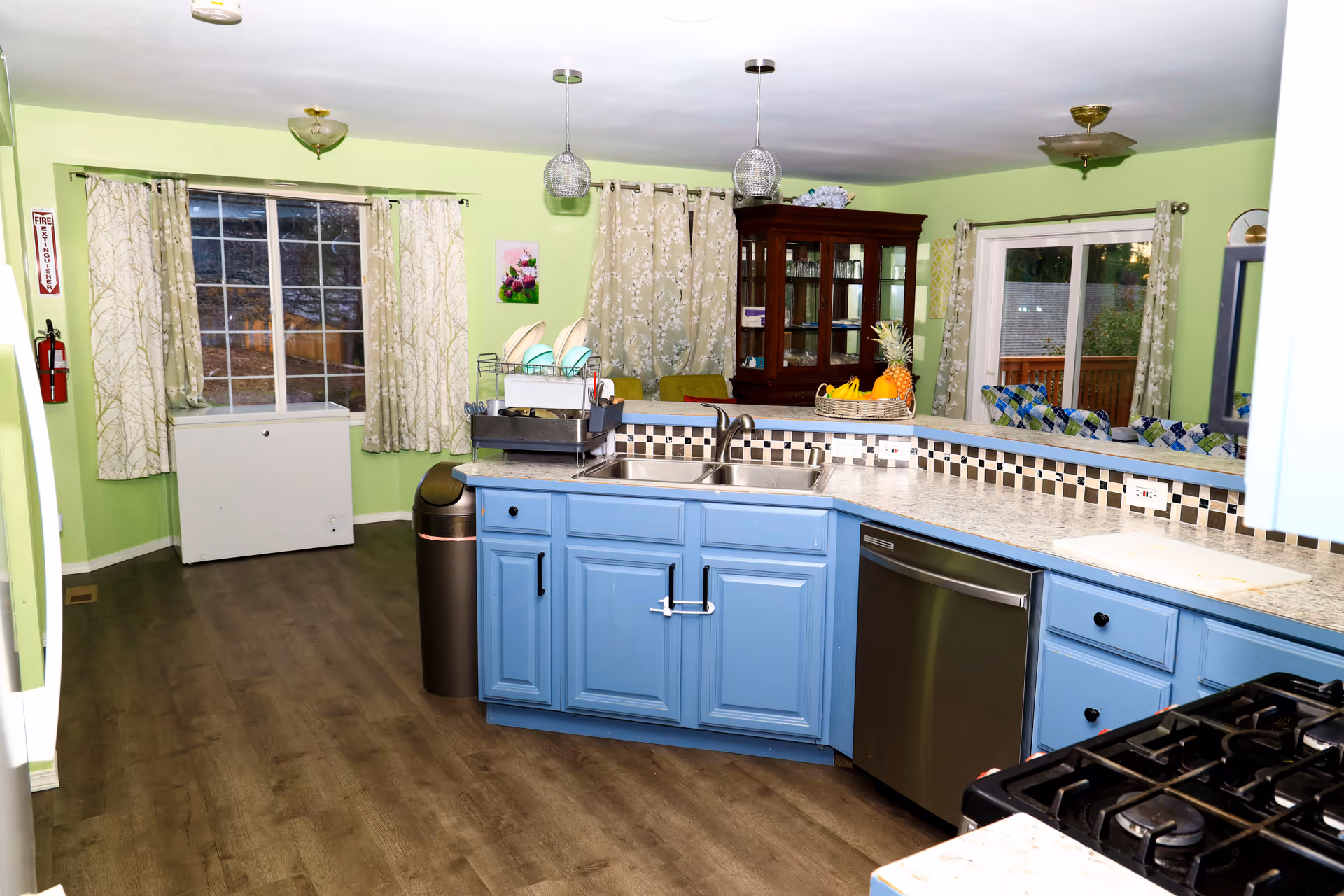 Bright lime green kitchen with blue cabinets, a long counter, sink, dish rack, and stainless appliances.