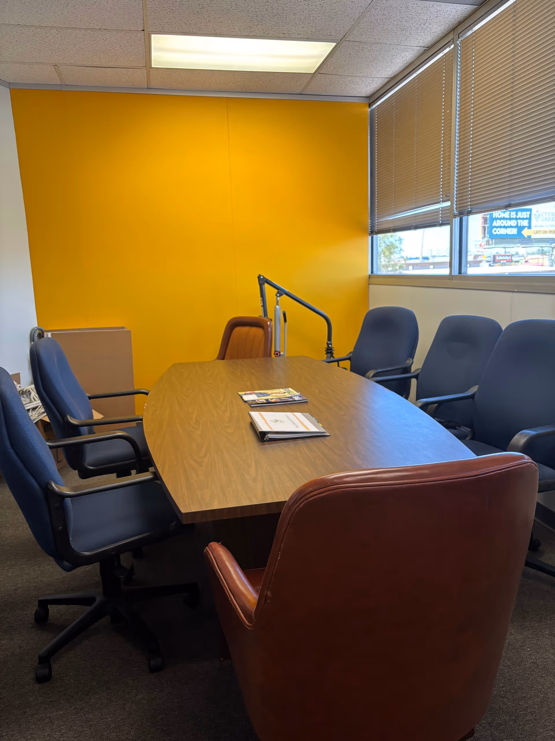 A conference room with a long wooden table, blue chairs, and a yellow wall.
