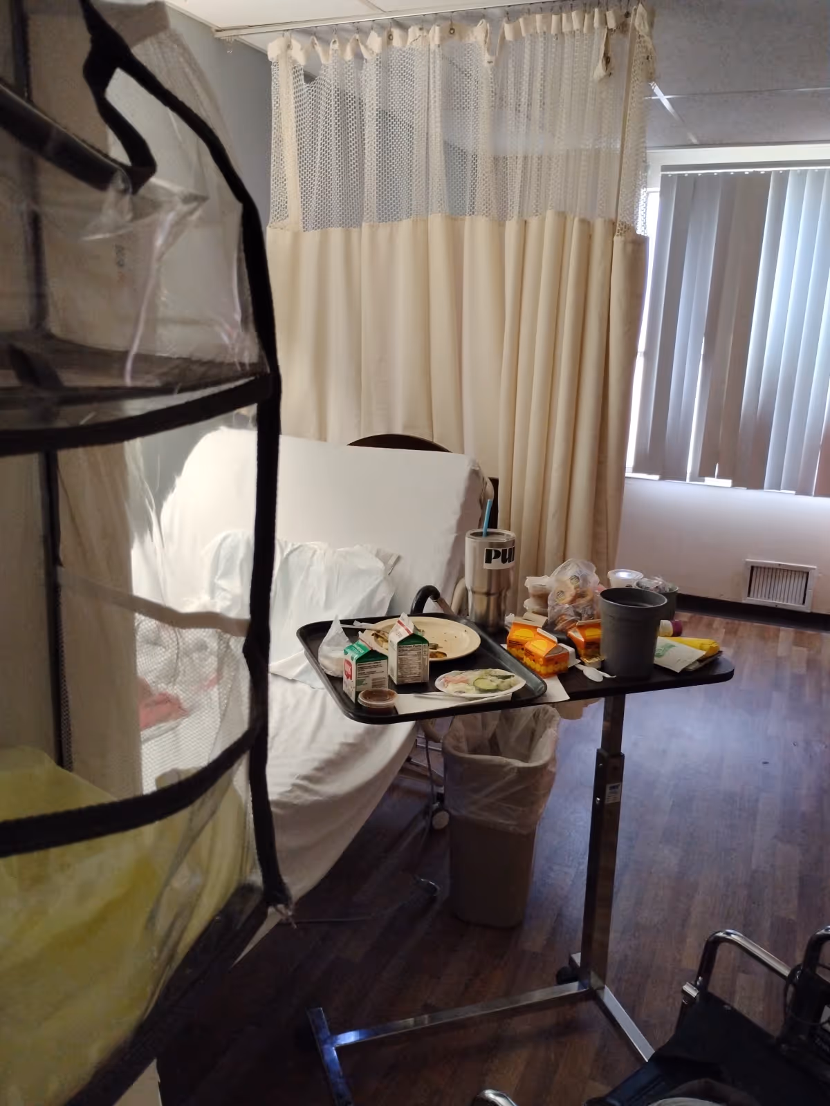 A hospital-style patient room with a bed, privacy curtain, and a tray table of snacks.