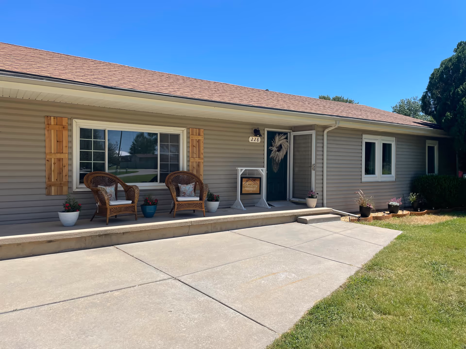 Single-story building with a front porch, wicker chairs, and potted plants outside.
