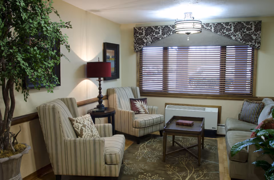 Comfortable living room with two striped armchairs, a sofa, coffee table, lamp, and a window with wooden blinds.