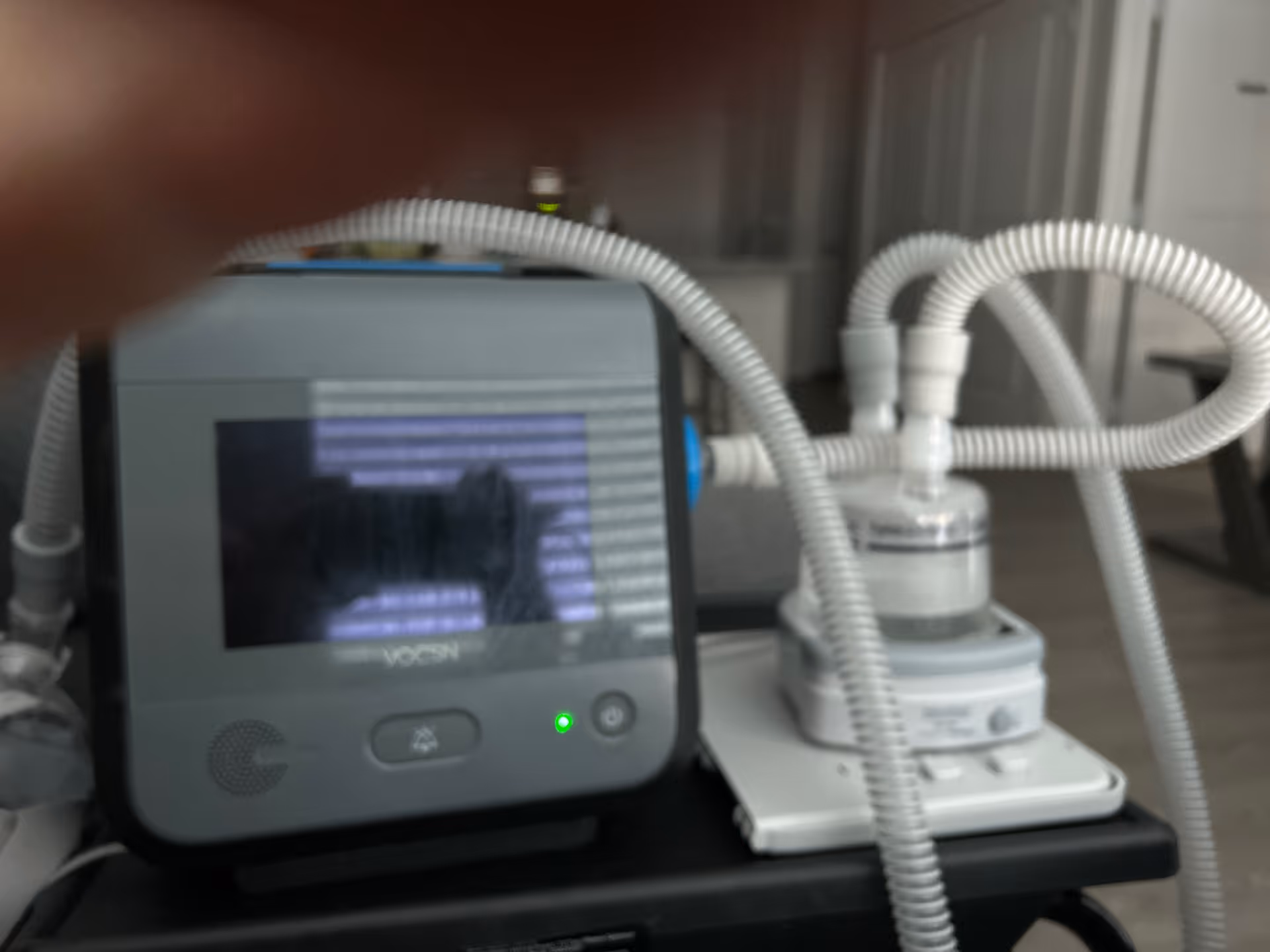 Close-up of a medical monitor and tubing on a cart in a clinical interior.