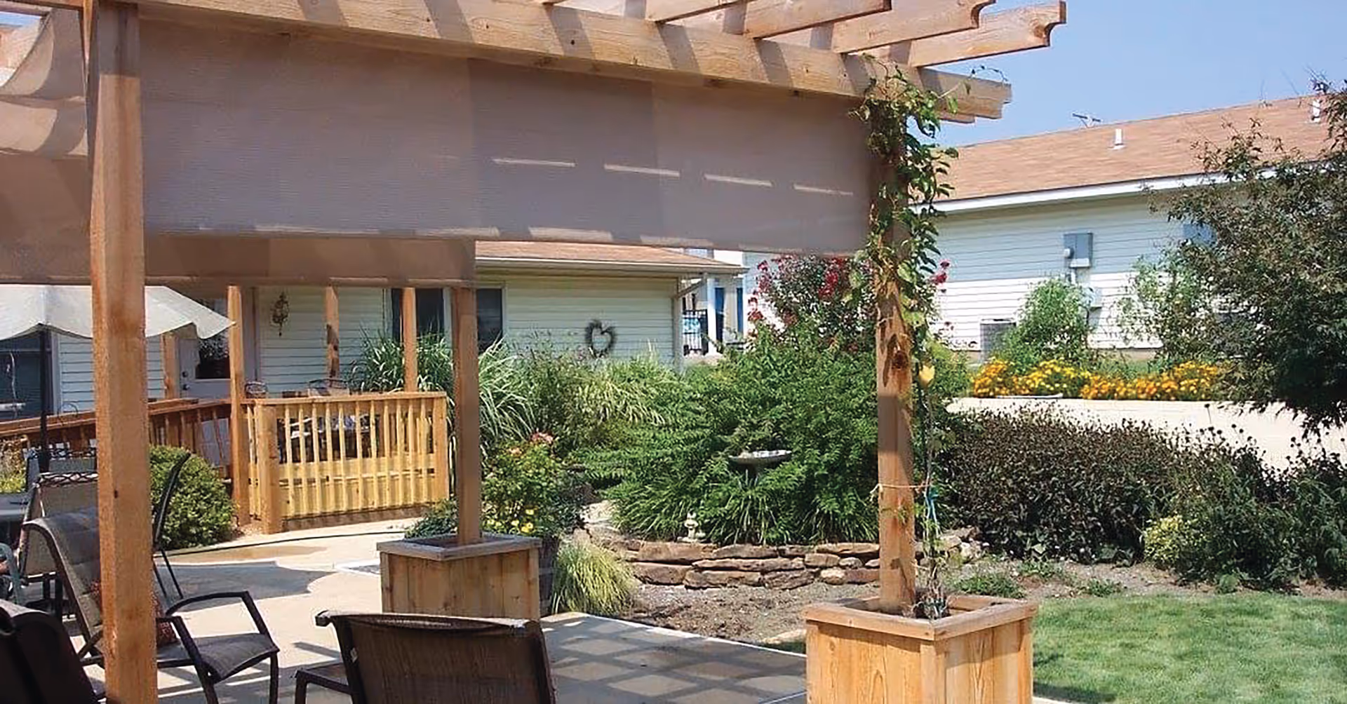 Outdoor patio with wooden pergola, seating, and landscaped garden at a senior living campus.