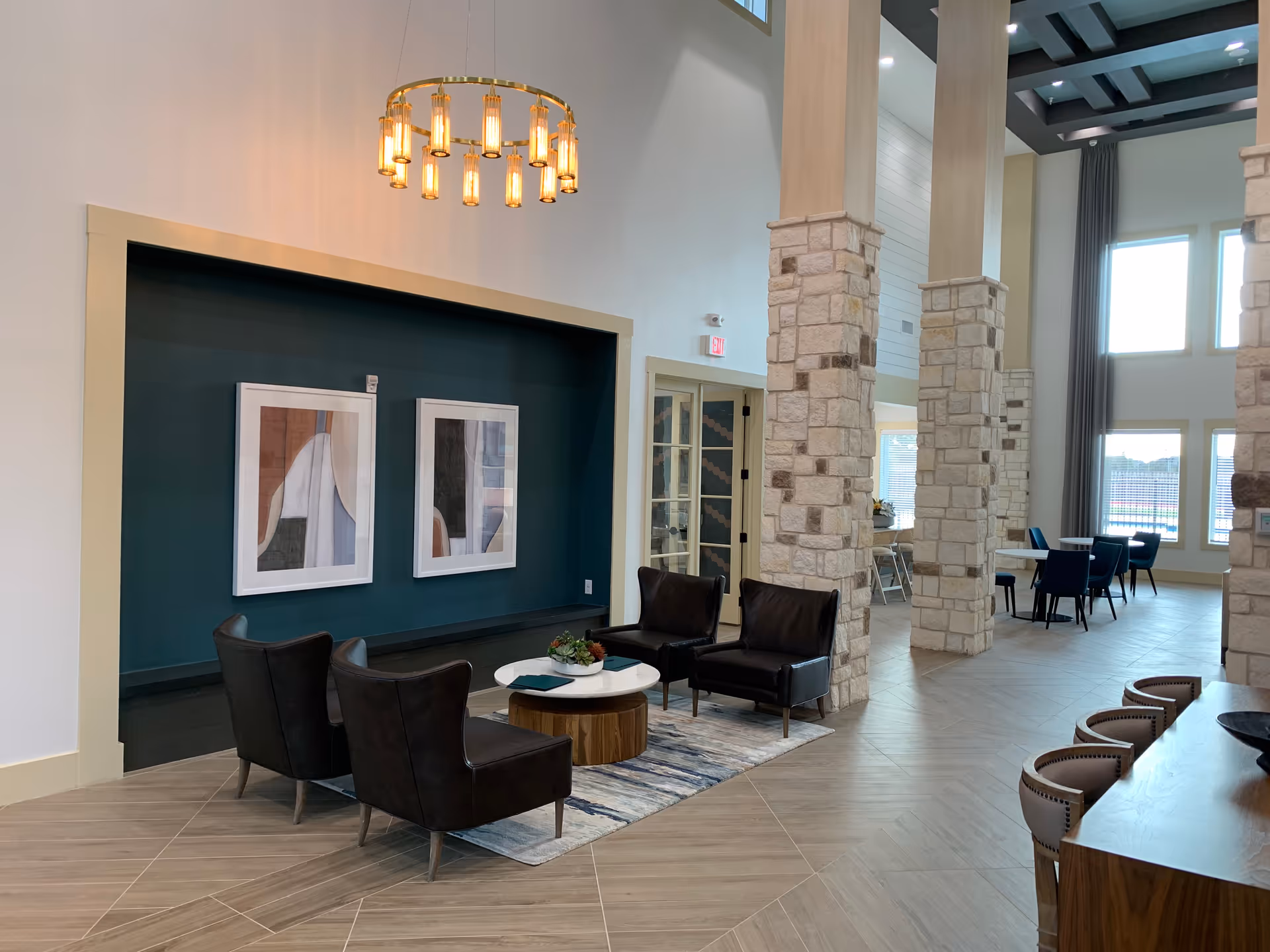 Modern lobby seating area with dark leather chairs, round coffee table, pillars, art, and chandelier.
