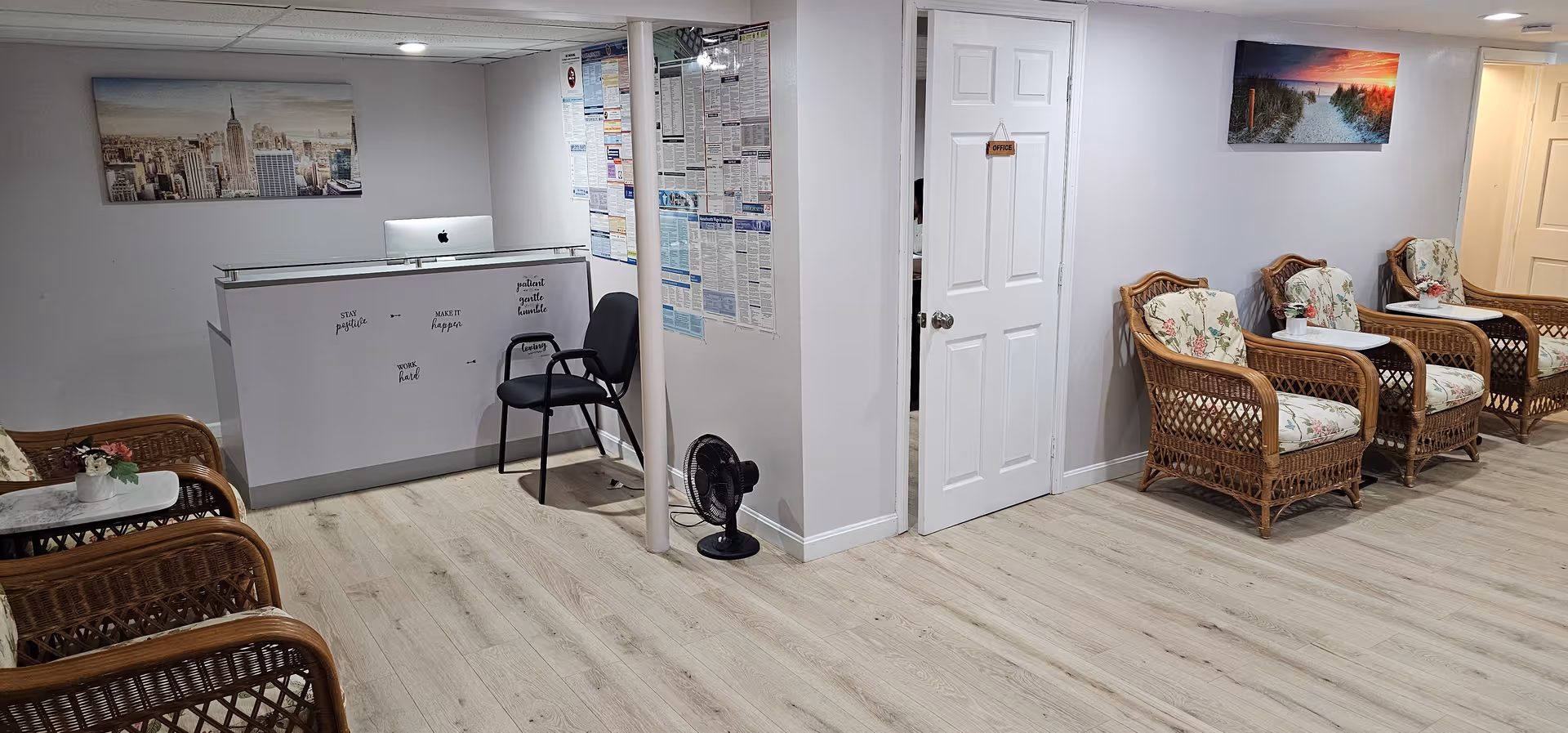 Reception lounge in a senior facility featuring wicker chairs, a front desk, and bulletin boards.