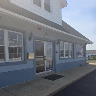 Exterior view of a light blue building entrance with windows and a sidewalk.