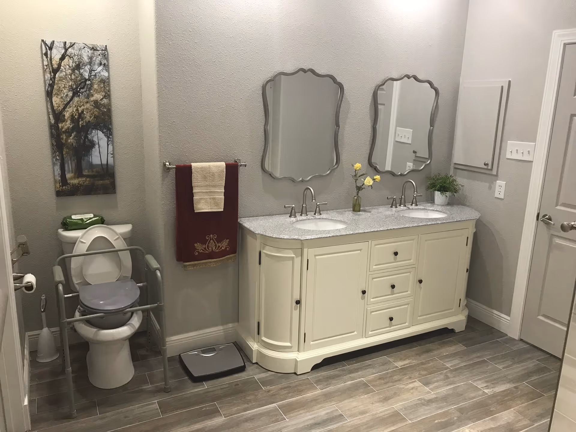 Bathroom with double vanity, mirrors, towel rack, and accessible toilet in a senior living facility.