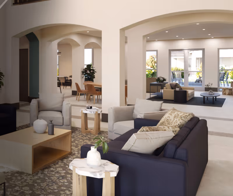 Open, modern lounge area with arched entryways, sofas, and large windows in a senior living lobby.