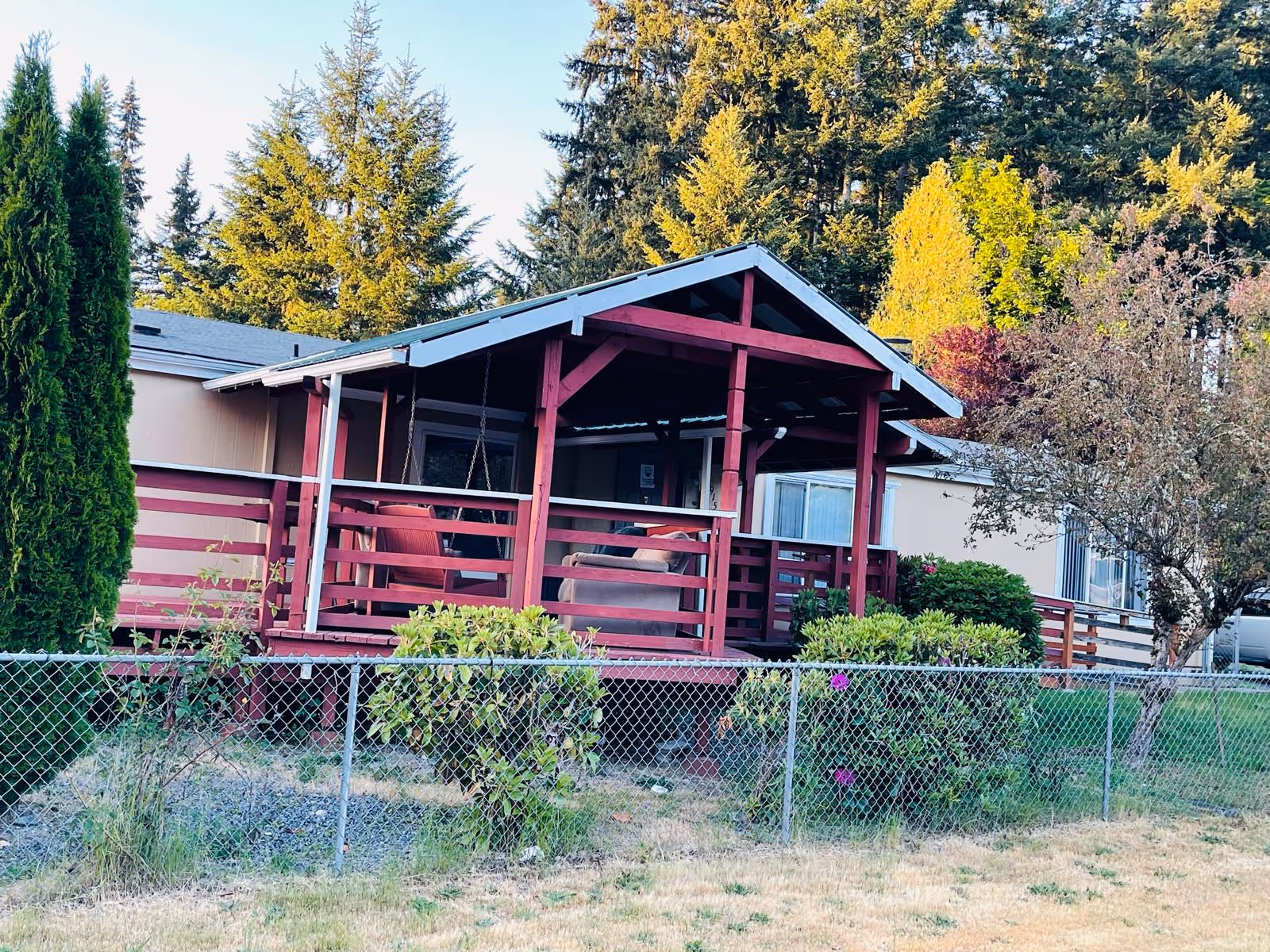 Red wooden porch with seating extends from a single-story building behind a chain-link fence.