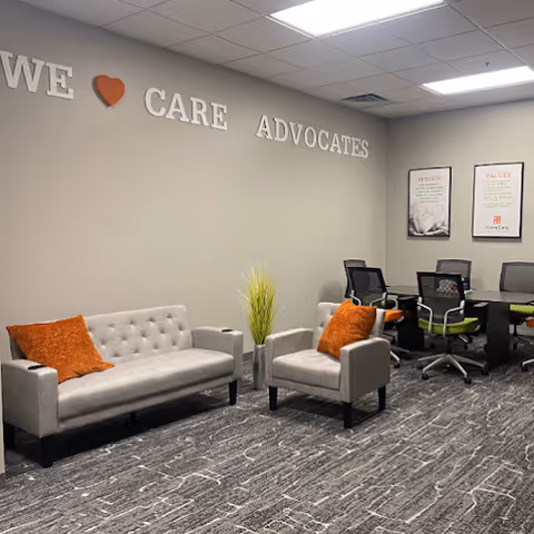 Modern waiting area with gray sofas, orange pillows, and a conference table.