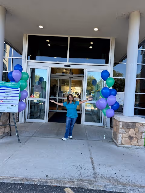 Staff member stands at the front entrance of A Place At Home, balloons decorate the doorway.