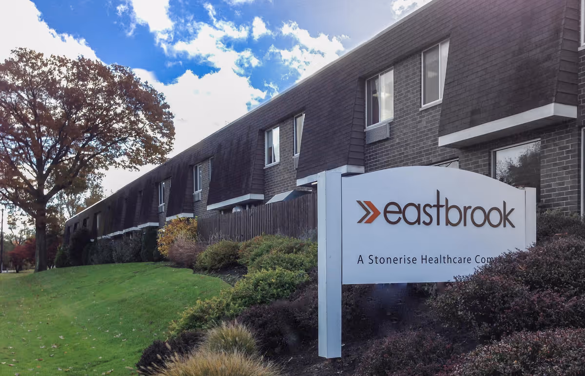 Exterior view of a long brick senior healthcare building with landscaping and a prominent sign reading "eastbrook".