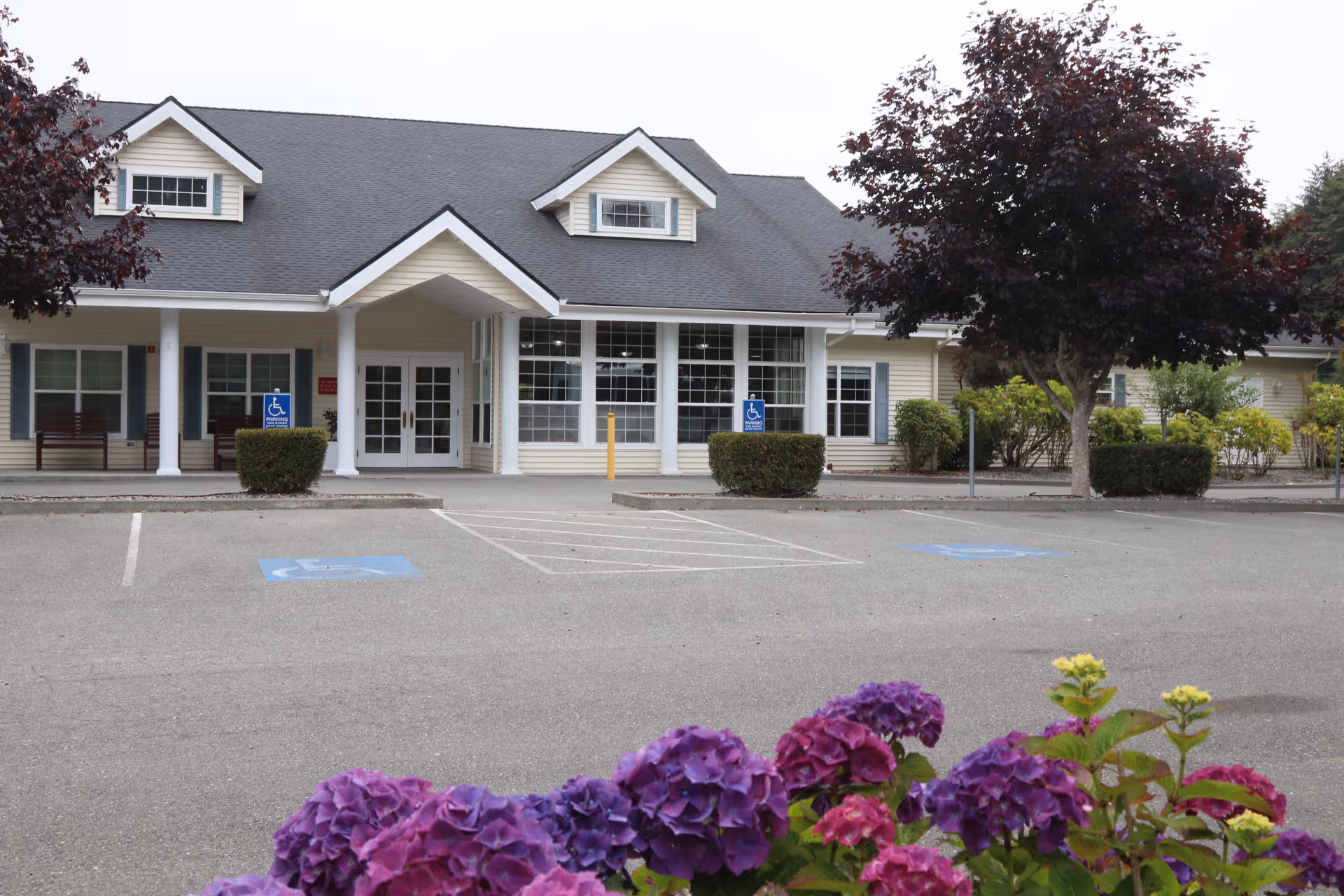 Senior living facility exterior with entrance, parking, and landscaped shrubs.