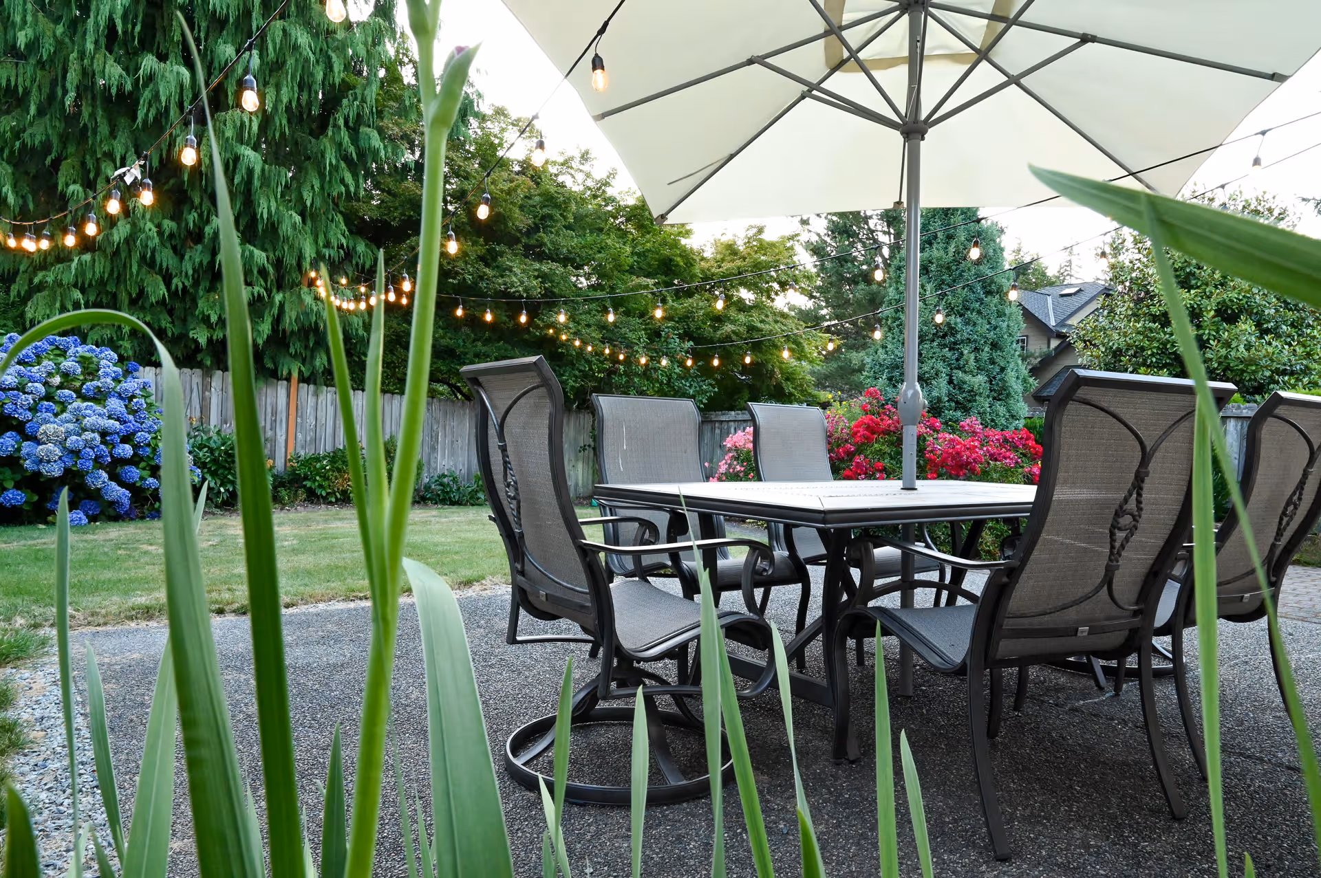 Outdoor patio with a table, chairs, umbrella, and string lights in a garden.