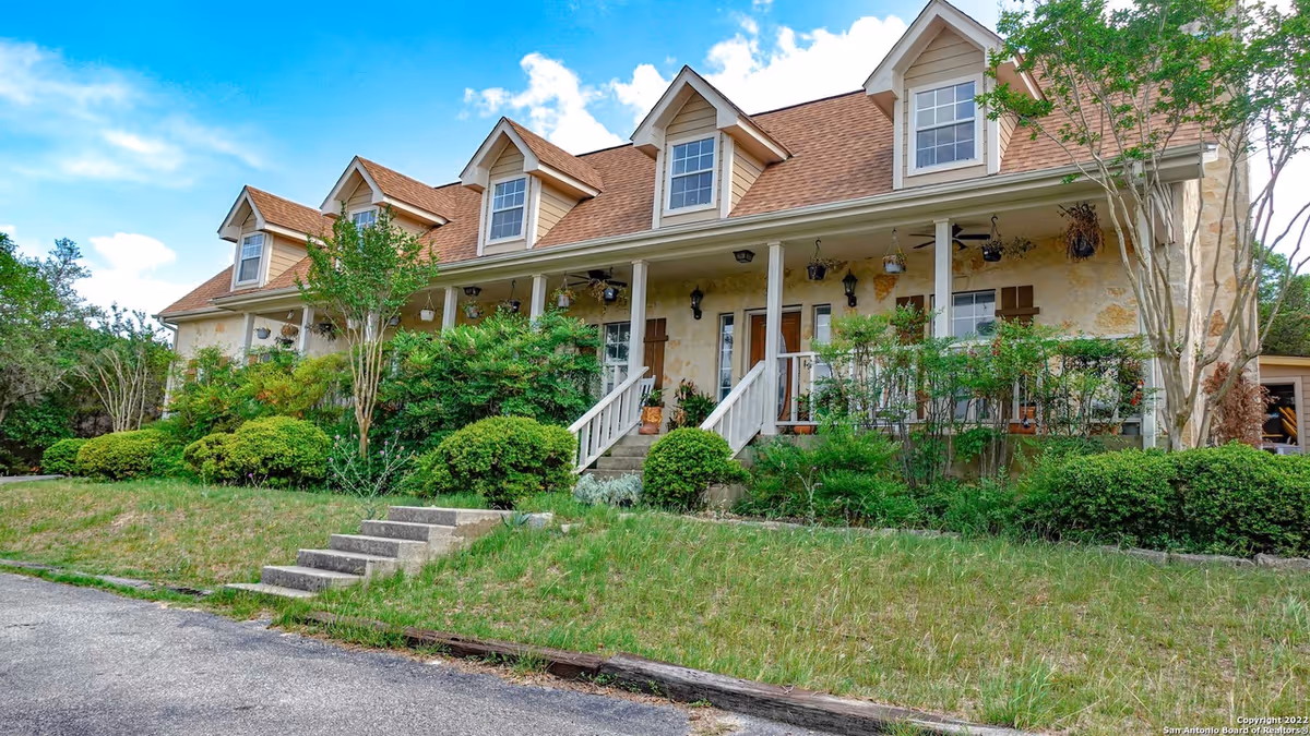 Exterior view of a two-story dormer-roofed building with a covered front porch and landscaped yard.