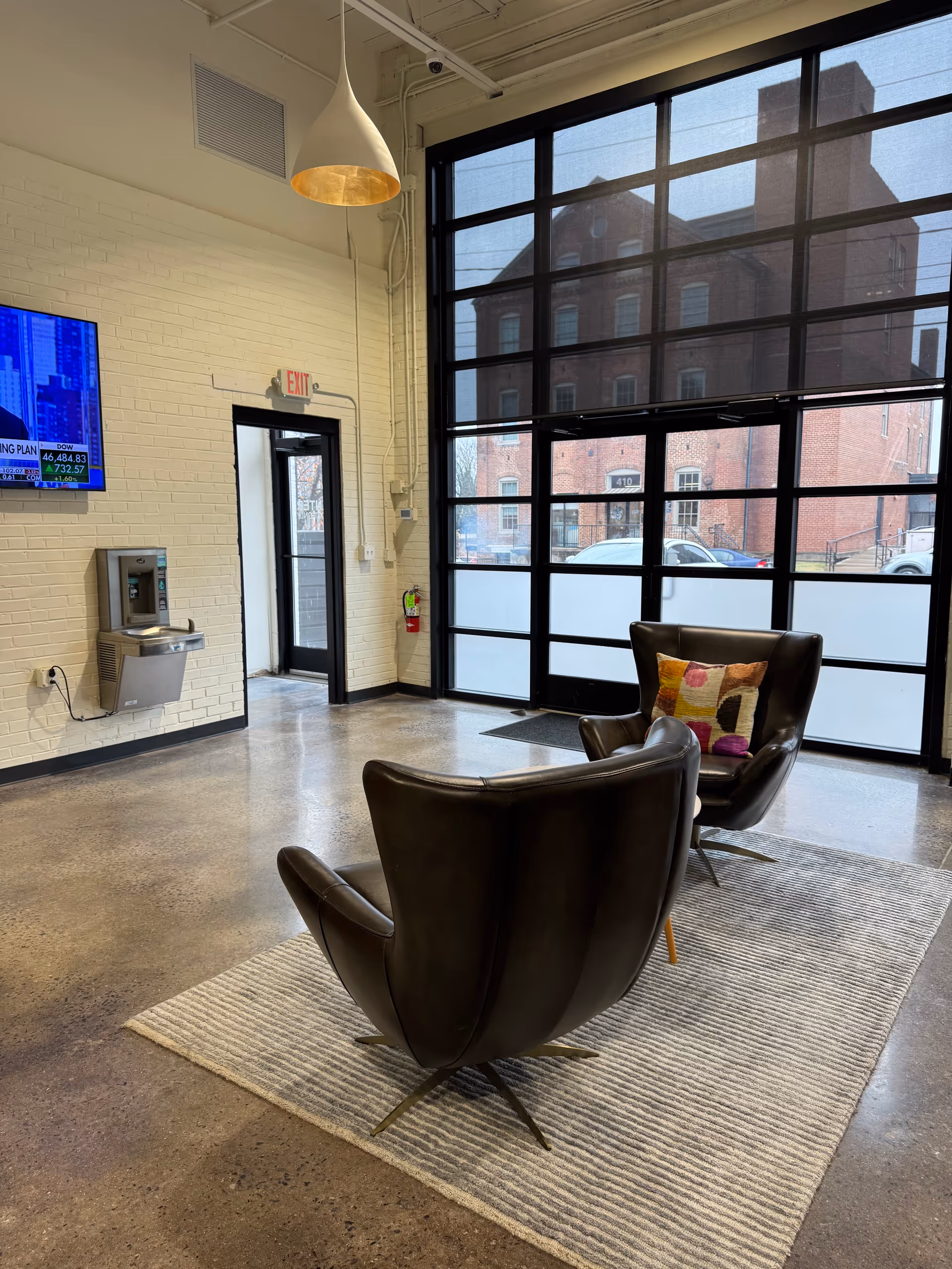 Modern facility lobby with two leather chairs, large glass windows, and a rug.