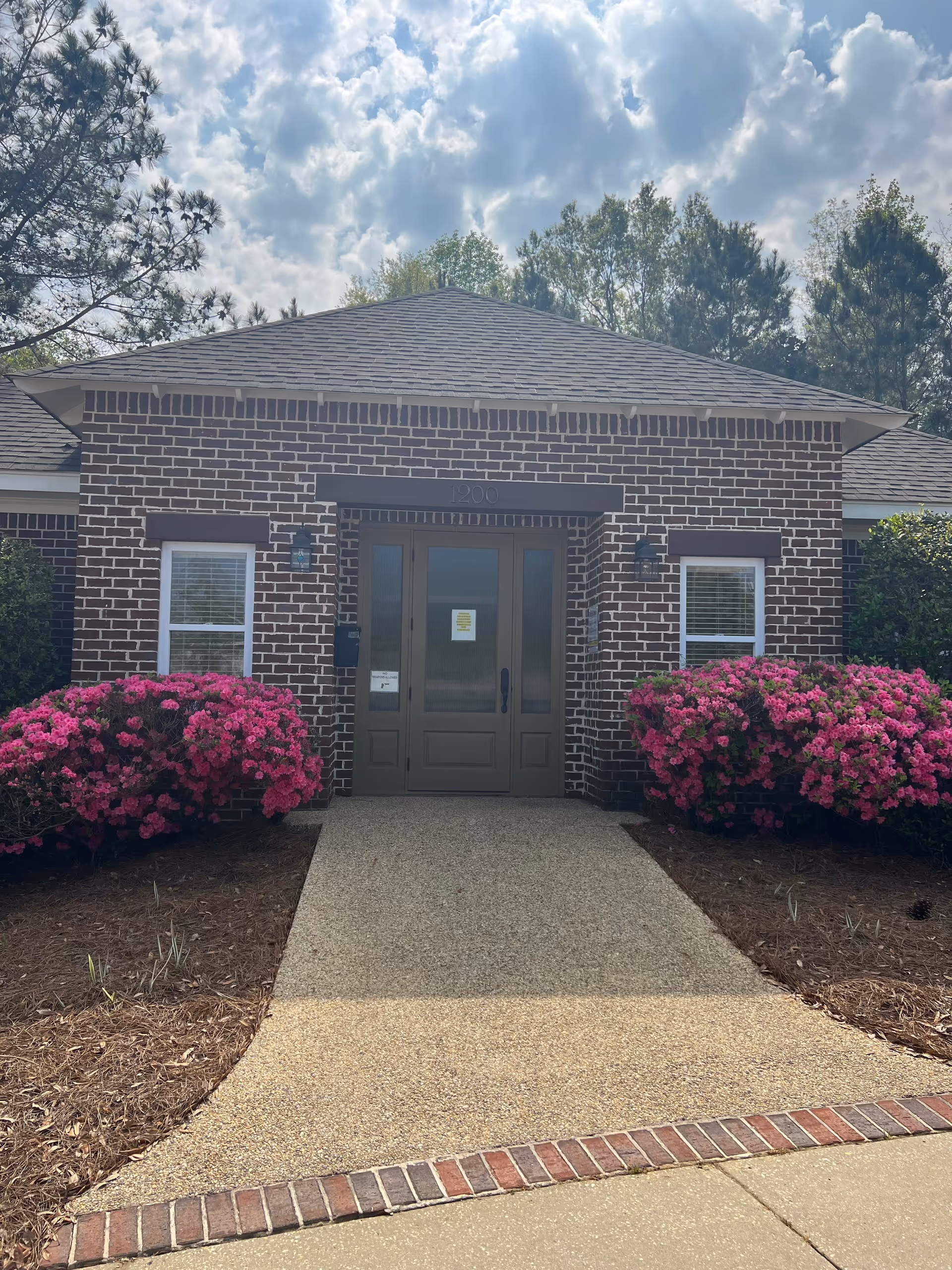 Brick building entrance with double doors, pink flowering shrubs, and a curved walkway.