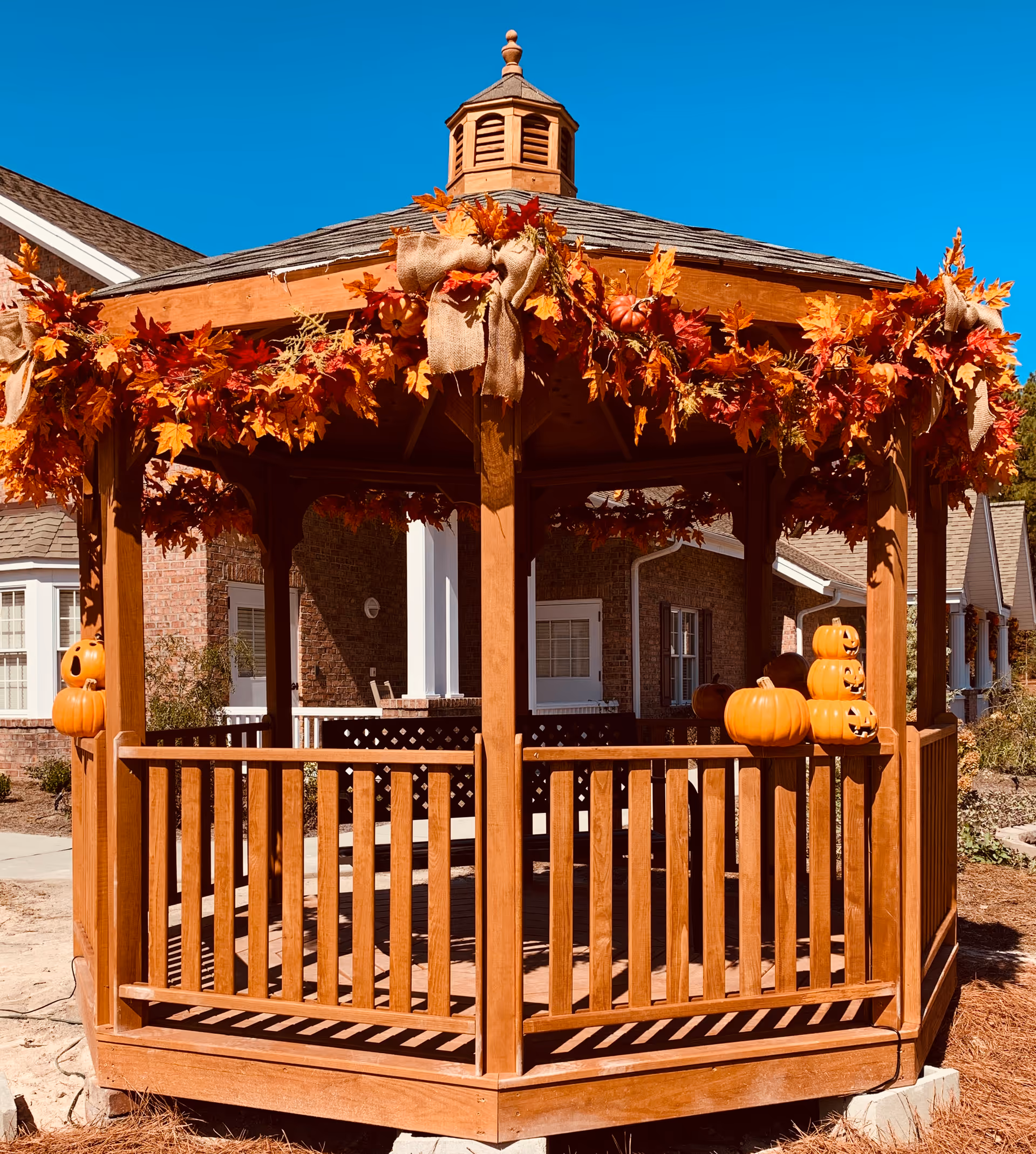 Wooden gazebo decorated with autumn leaves and pumpkins in front of a brick house