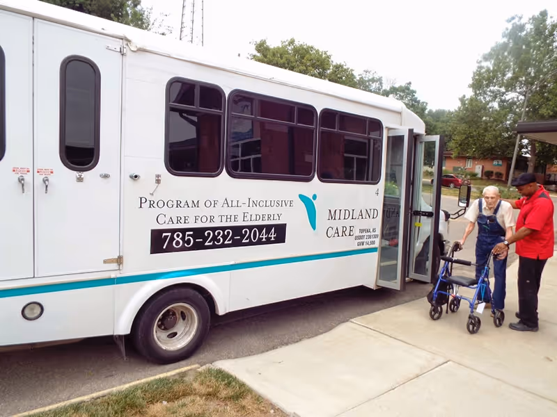 A white Midland Care shuttle van parked curbside with a walker-assisted senior and caregiver.