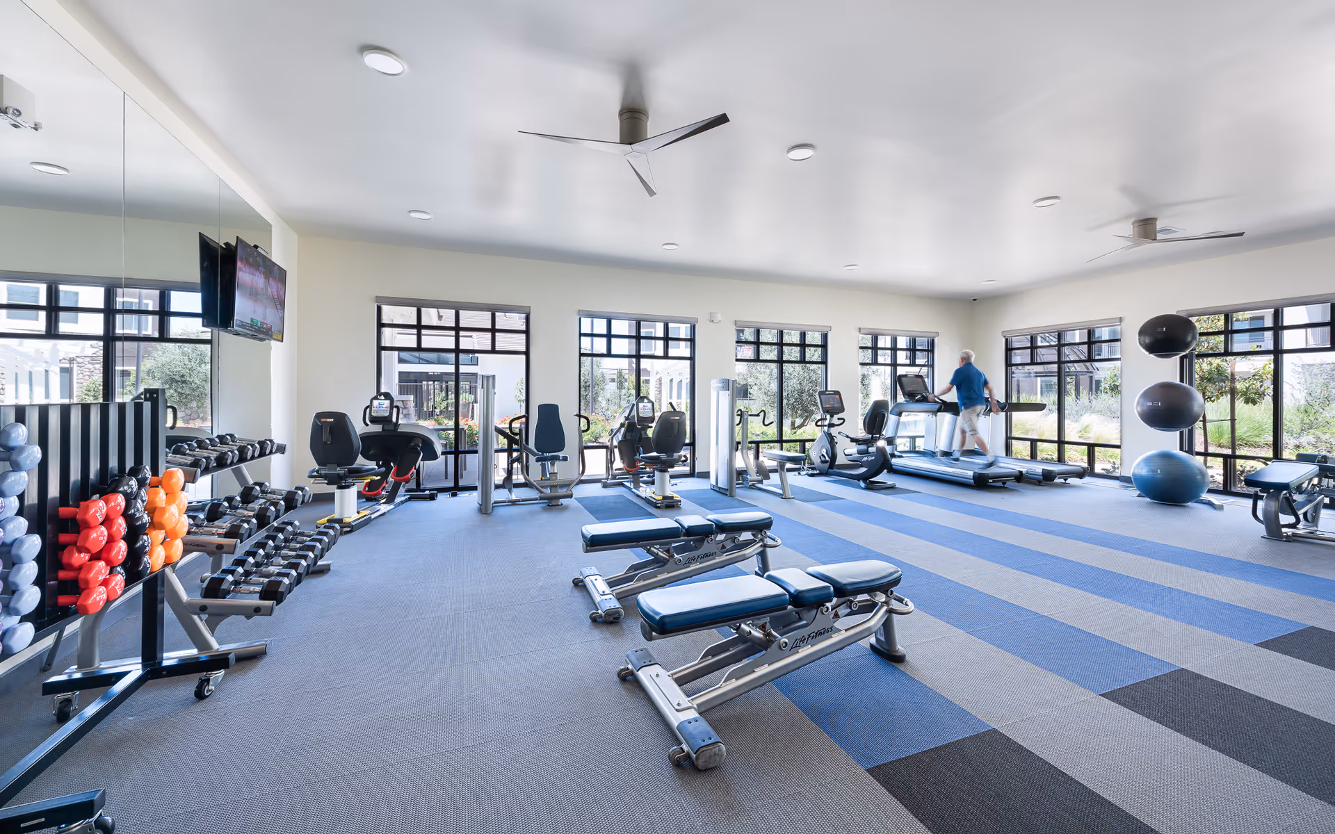 Well-equipped senior fitness center with treadmills, weights, benches, and large windows.