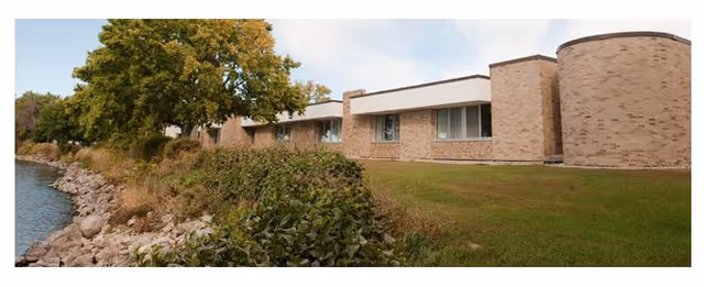 Exterior view of a brick senior living facility beside a river with trees.