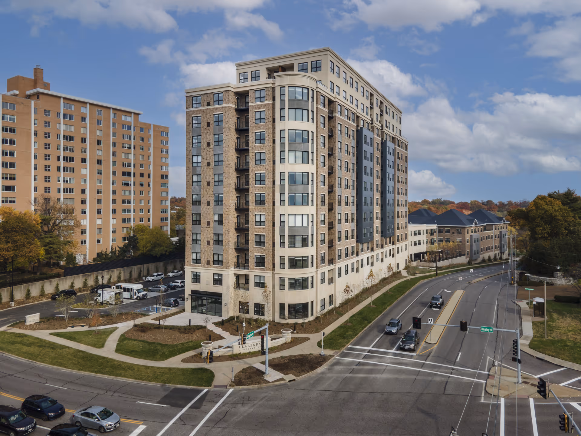 A modern multi-story senior living building sits at a busy street corner with parked cars.