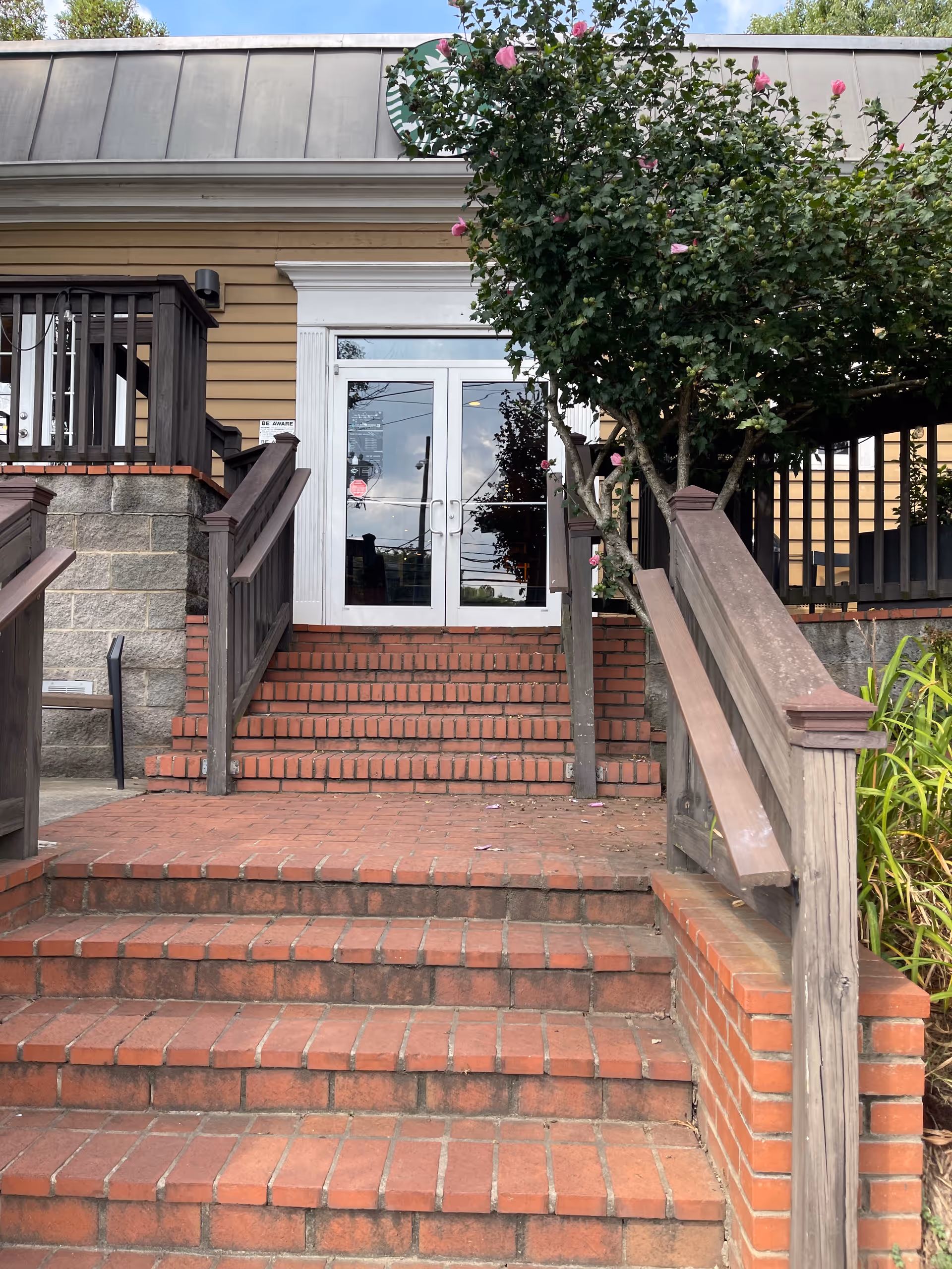 Brick stairs lead to glass double doors at a senior facility entrance, with a tree nearby.