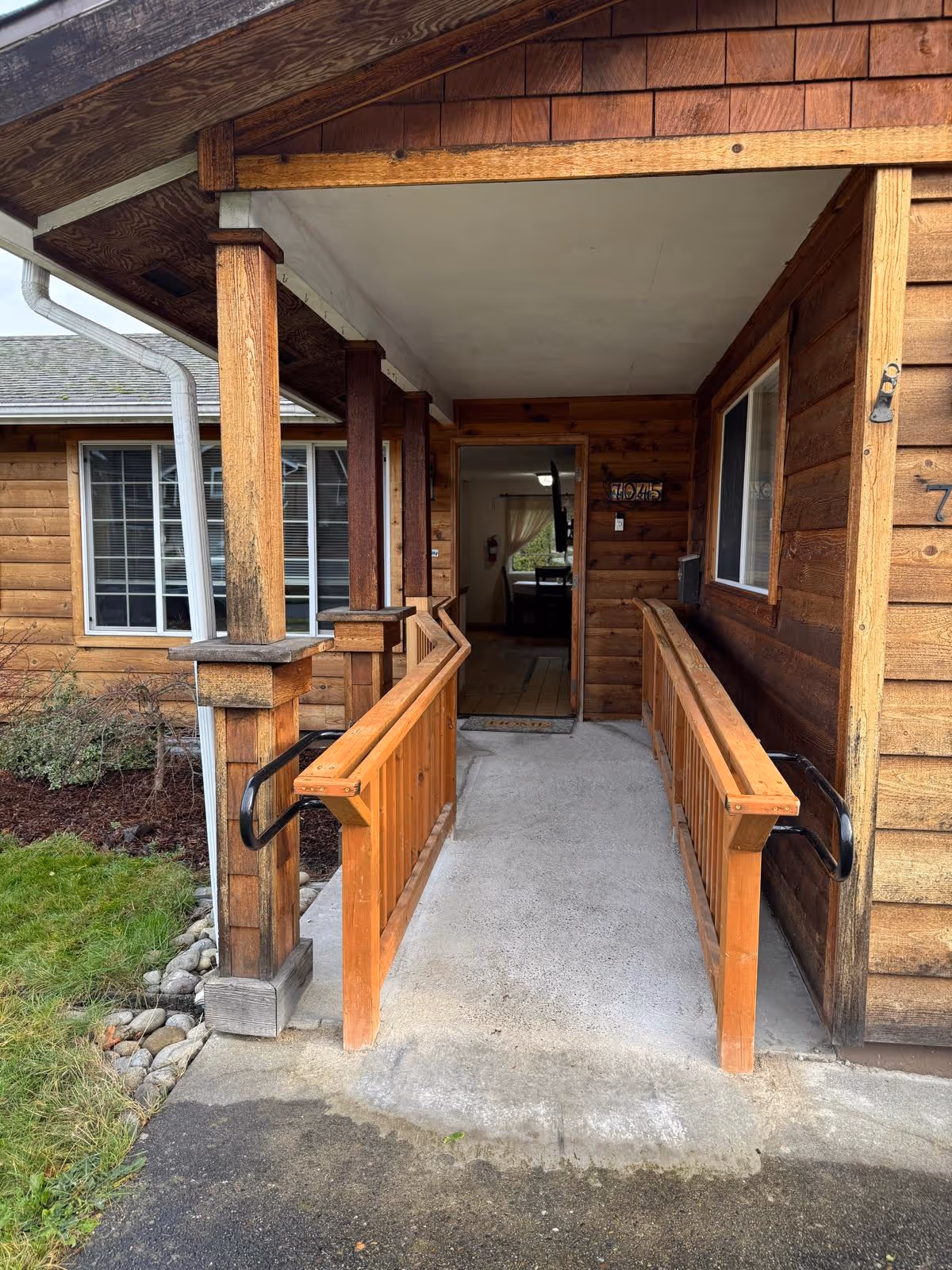 Wooden exterior entrance of a senior living home with a ramp and railing.