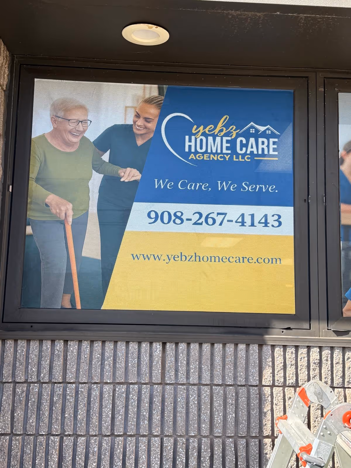 Blue and yellow window banner displaying Yebz Home Care Agency with caregiver assisting a senior.