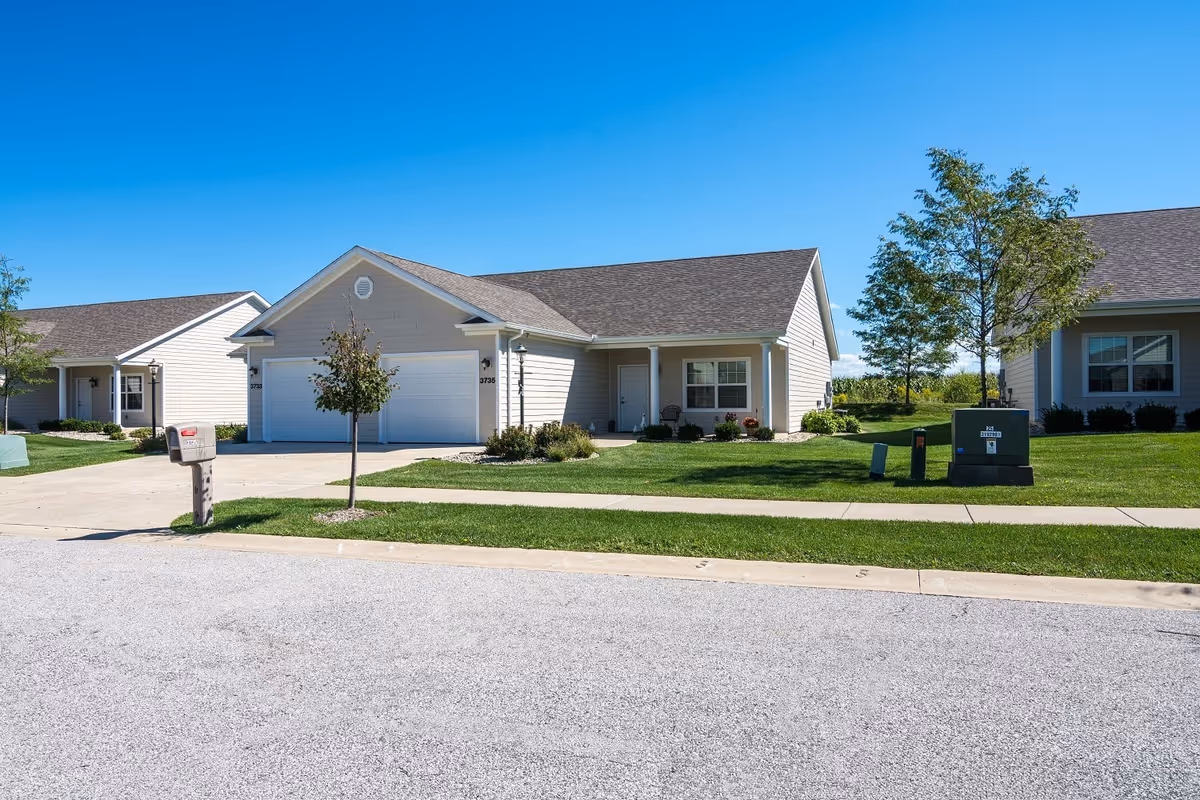 Single-story ranch-style homes with garages, driveways, a mailbox and well-kept lawns under a clear blue sky.